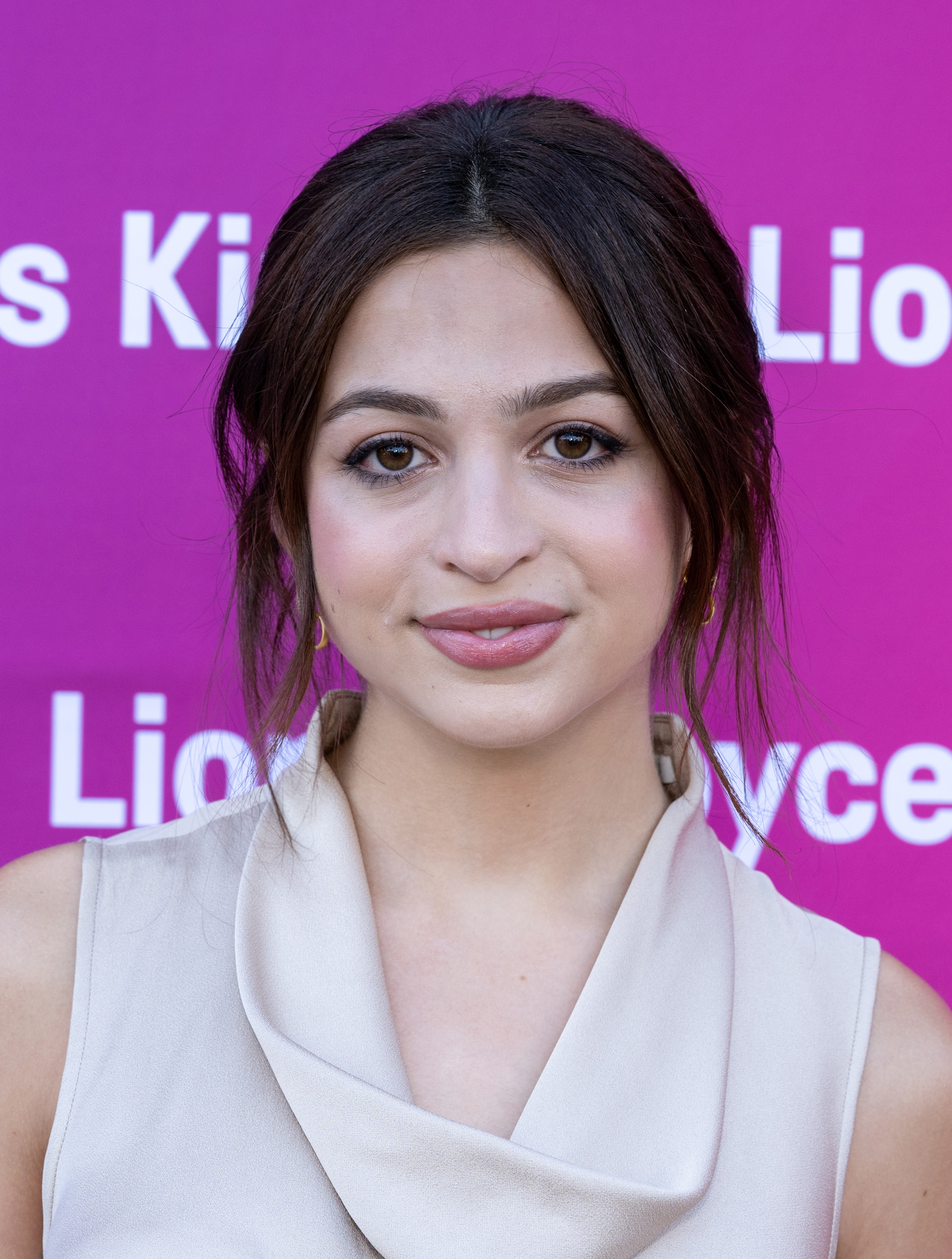 Josie Totah posa en el evento "Film Independent New Wave Actors Panel and Conversation" con un conjunto sin mangas de color claro y escote drapeado. Lleva el pelo oscuro recogido en un moño suelto, con algunos mechones que le enmarcan la cara. | Fuente: Getty Images