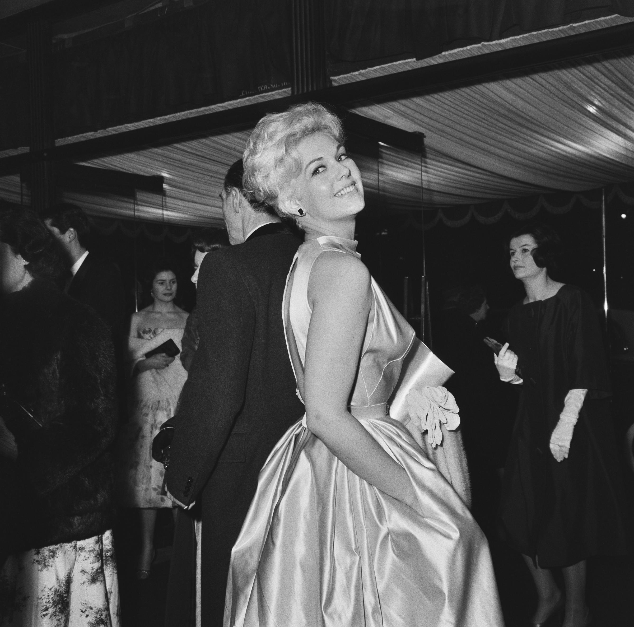 Kim Novak asiste a la función real de "Once More, with Feeling" en el Odeon Leicester Square de Londres, con un vestido de satén sin mangas y sonriendo por encima del hombro. | Fuente: Getty Images