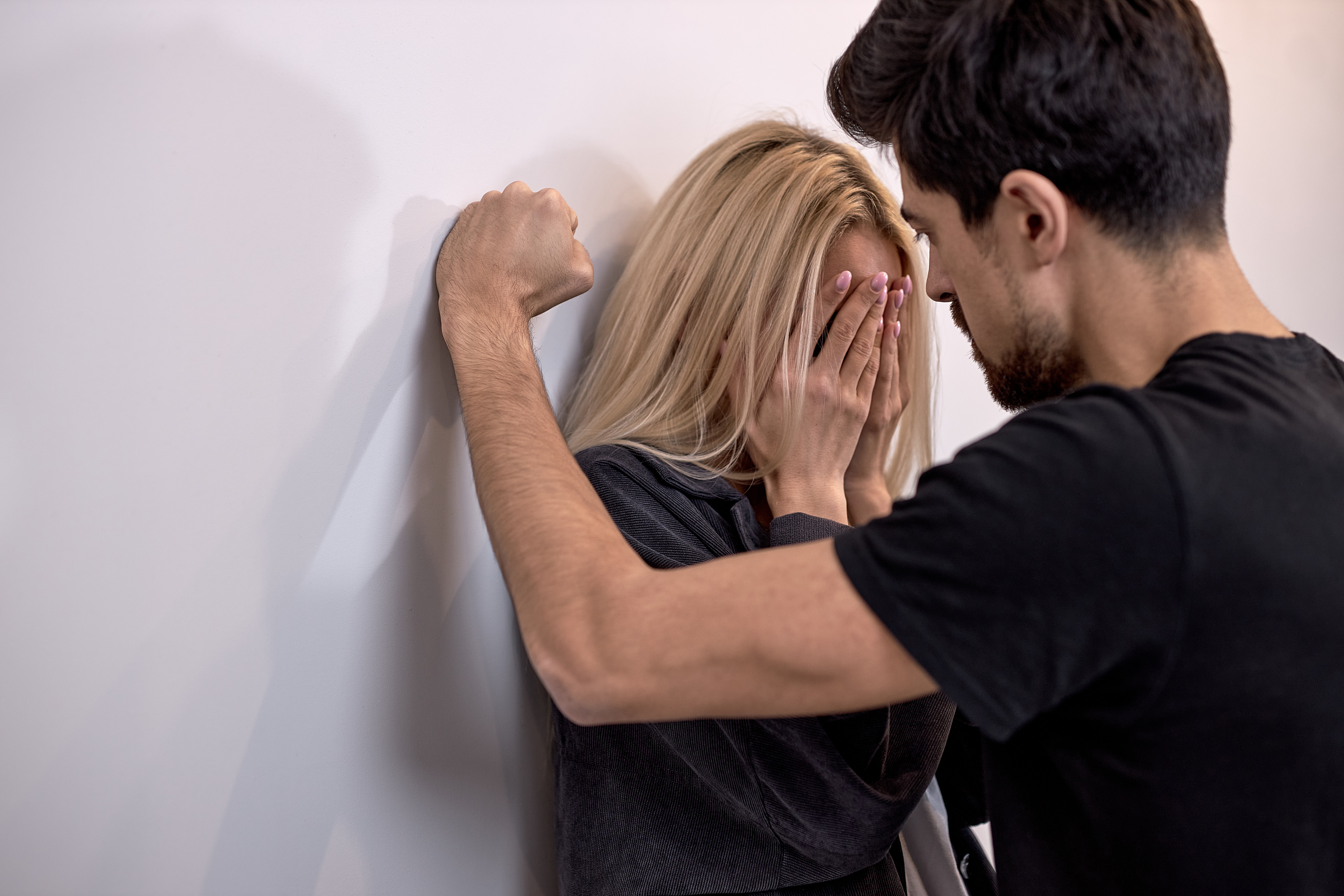 Una mujer de pie contra una pared oculta su rostro mientras un hombre se sitúa frente a ella con el brazo apoyado en la pared. | Foto: Shutterstock