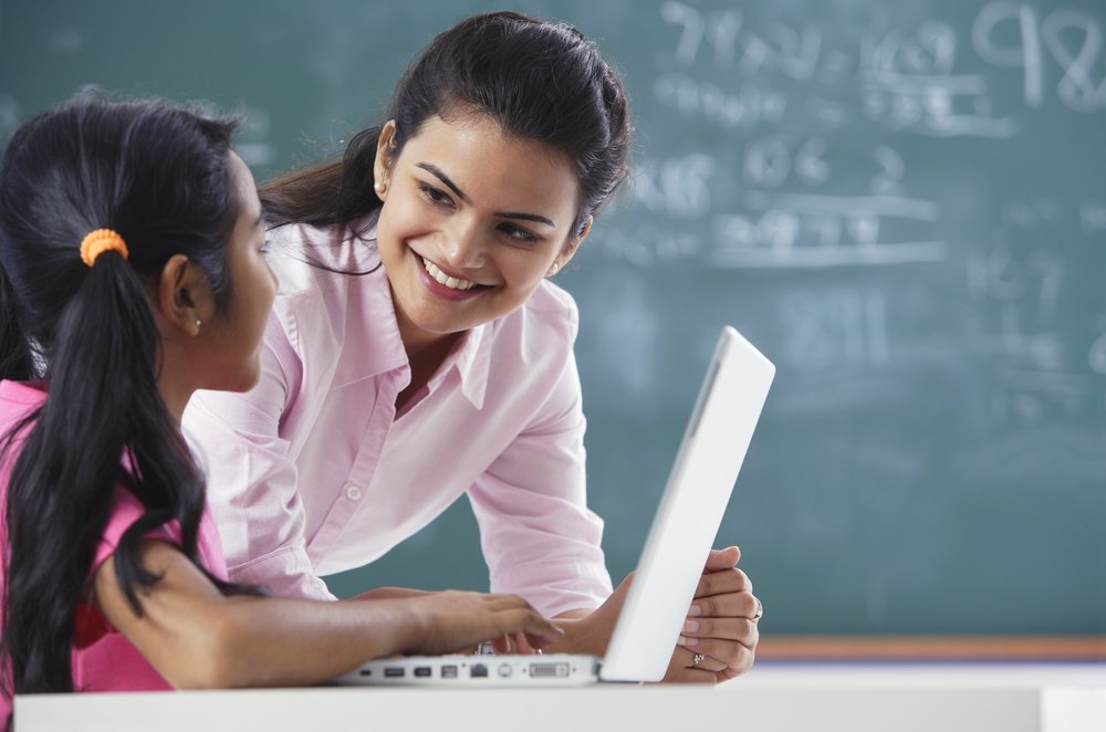 Maestra enseñando a una alumna con una laptop. | Fuente: Shutterstock