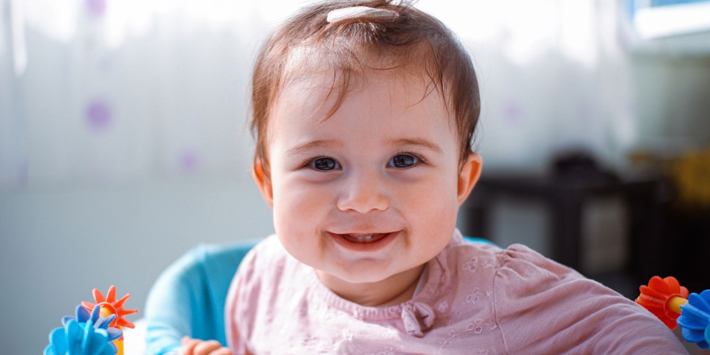 Una niña sonriente sentada en una sillita de actividades de colores | Fuente: Pexels