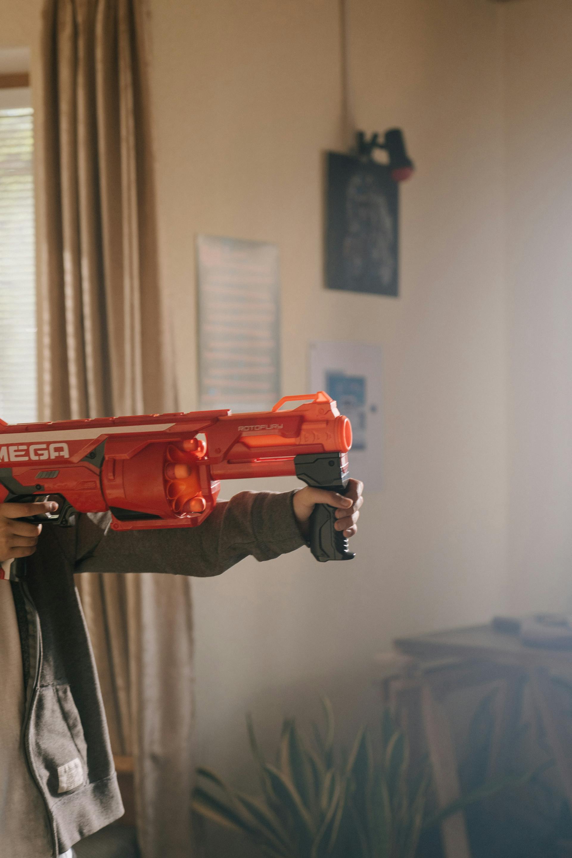 Primer plano de un niño sosteniendo una pistola roja de juguete | Fuente: Pexels