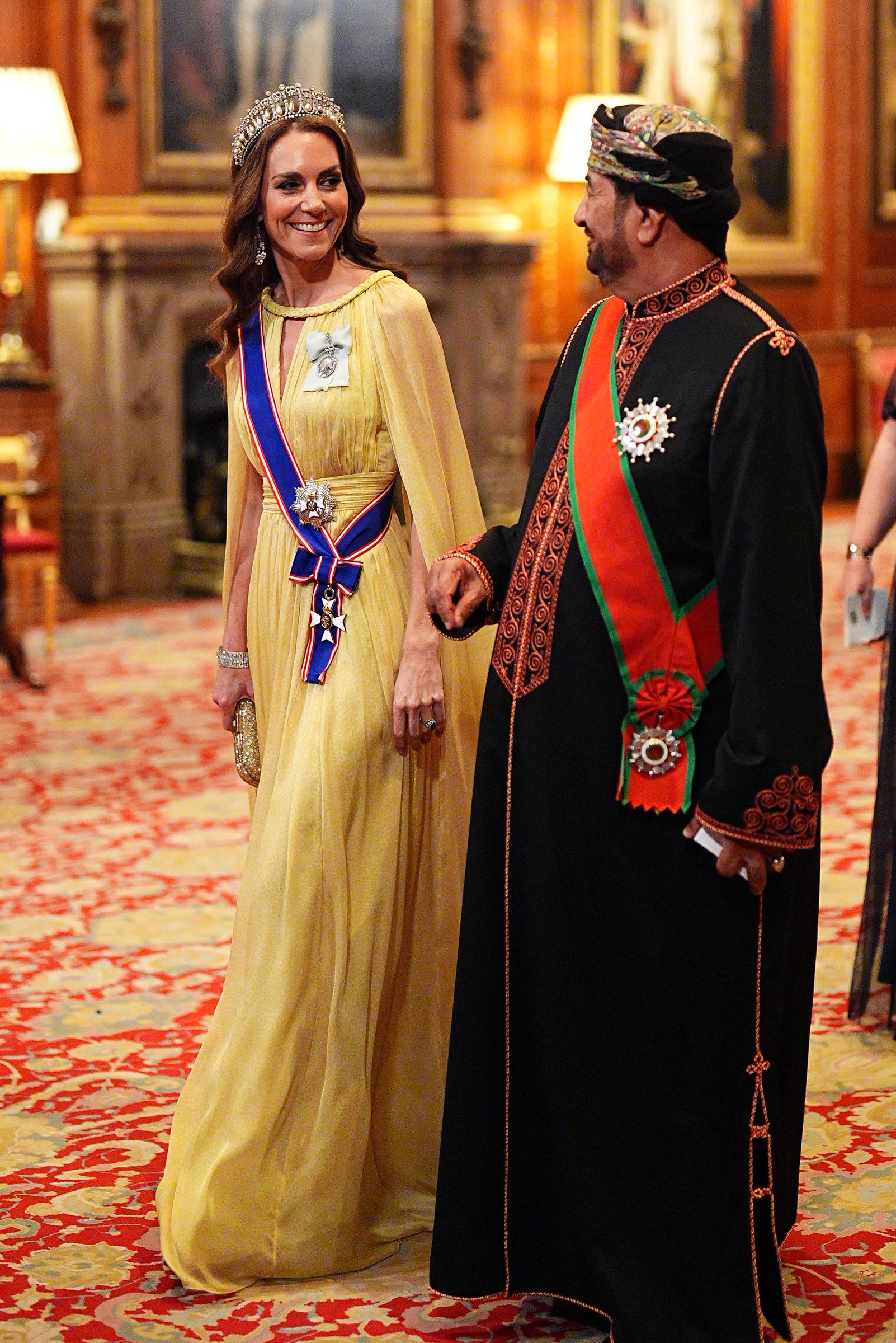 Catherine, princesa de Gales, sonríe y conversa con S. E. Sayyid Khalid Hilal Al Busaidy mientras avanzan en procesión hacia el banquete de Estado en el castillo de Windsor el 20 de octubre de 2026. La princesa destaca con un vaporoso vestido amarillo de Elie Saab, con capa y cuello trenzado, y la tiara Lover's Knot de la reina Mary. El funcionario omaní viste un bisht tradicional con bordados dorados y rojos, banda ceremonial y un colorido turbante massar. | Fuente: Getty Images