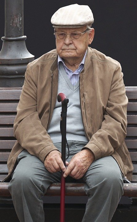 Anciano sentado en una banquilla sosteniendo un bastón. | Imagen: Max Pixel