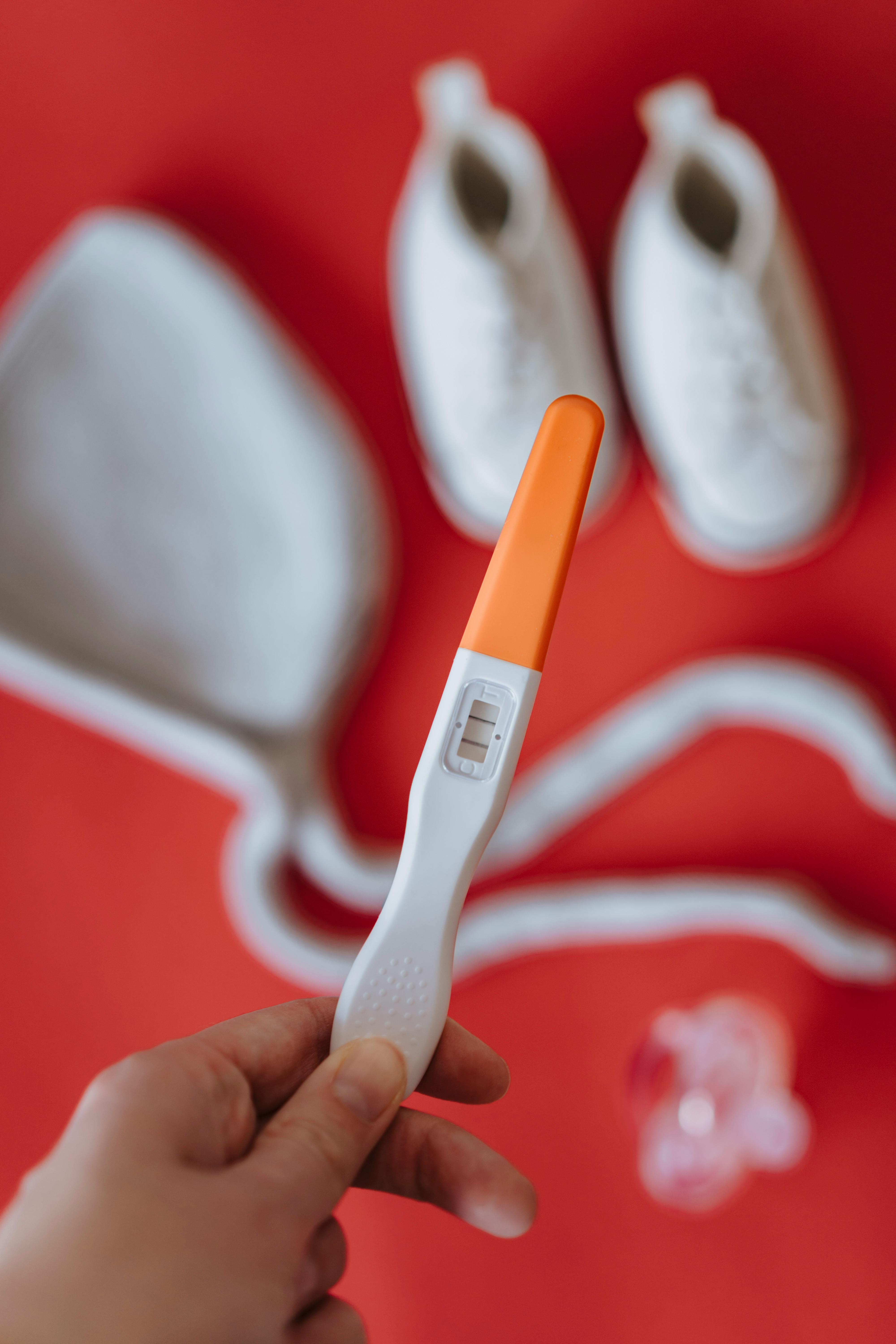 Alguien sostiene un test de embarazo positivo sobre ropa de bebé | Foto: Pexels