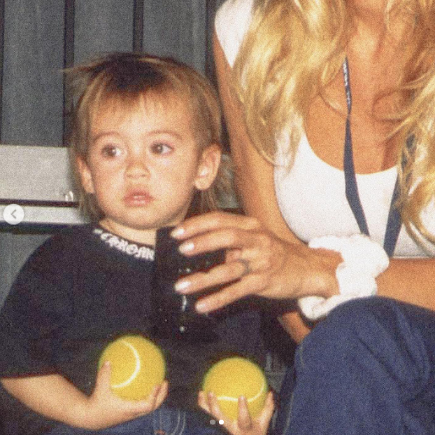 En una foto íntima de estilo retro, un joven Dylan Jagger Lee aparece sentado con dos pelotas de tenis amarillas en las manos, mientras su madre, Pamela Anderson, le rodea afectuosamente con un brazo, vestida con una camiseta sin mangas blanca y unos pantalones azules. Reflexionando sobre su experiencia como madre durante las vacaciones, celebró los sólidos cimientos de amor que sostienen su vida: "El amor… y el orgullo que siento, como madre de los maravillosos Brandon y Dylan… Mi historia de amor no estaría completa sin ellos. 🤍" | Fuente: Instagram/pamelaanderson