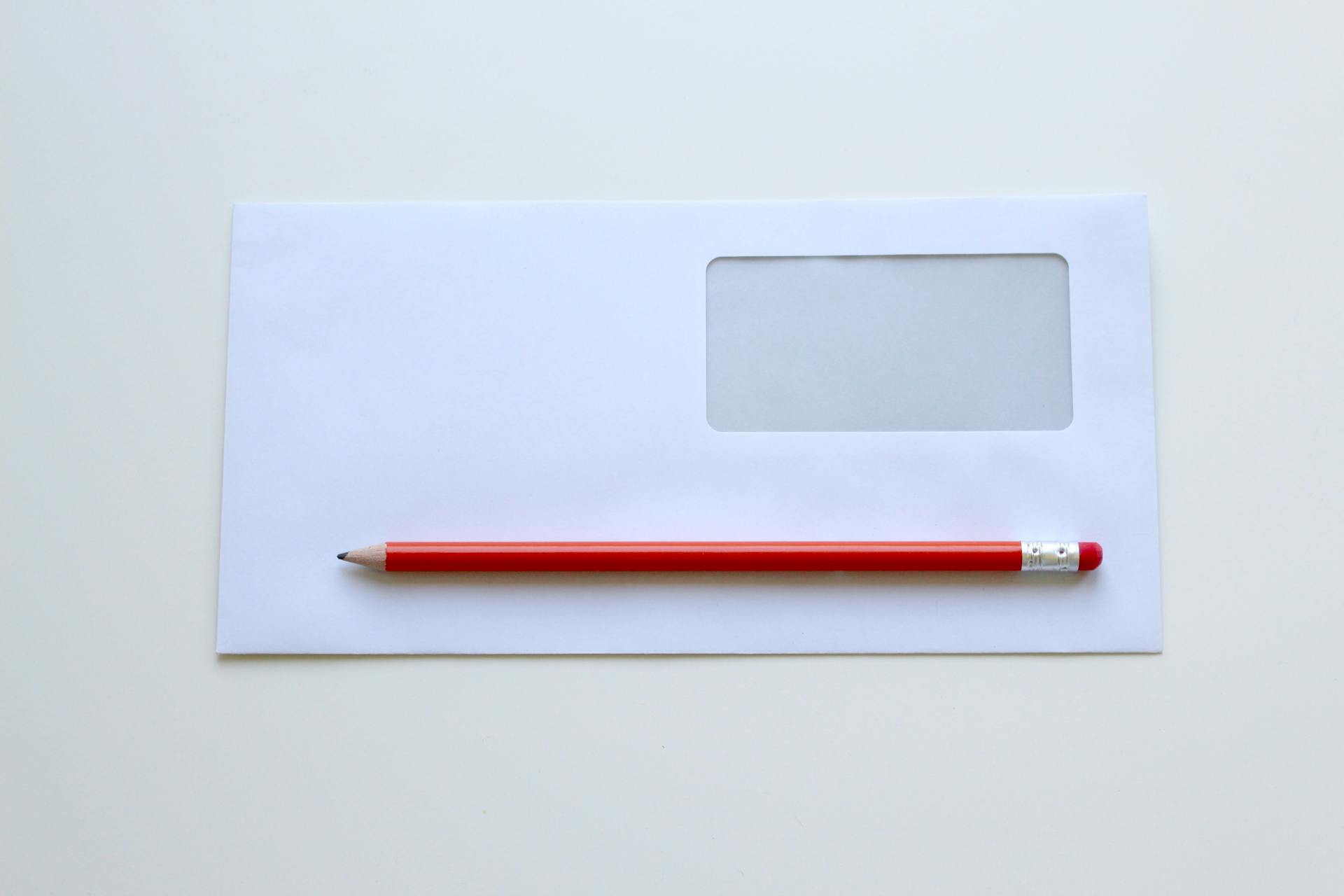 Un lápiz rojo sobre un sobre blanco con ventana | Fuente: Pexels