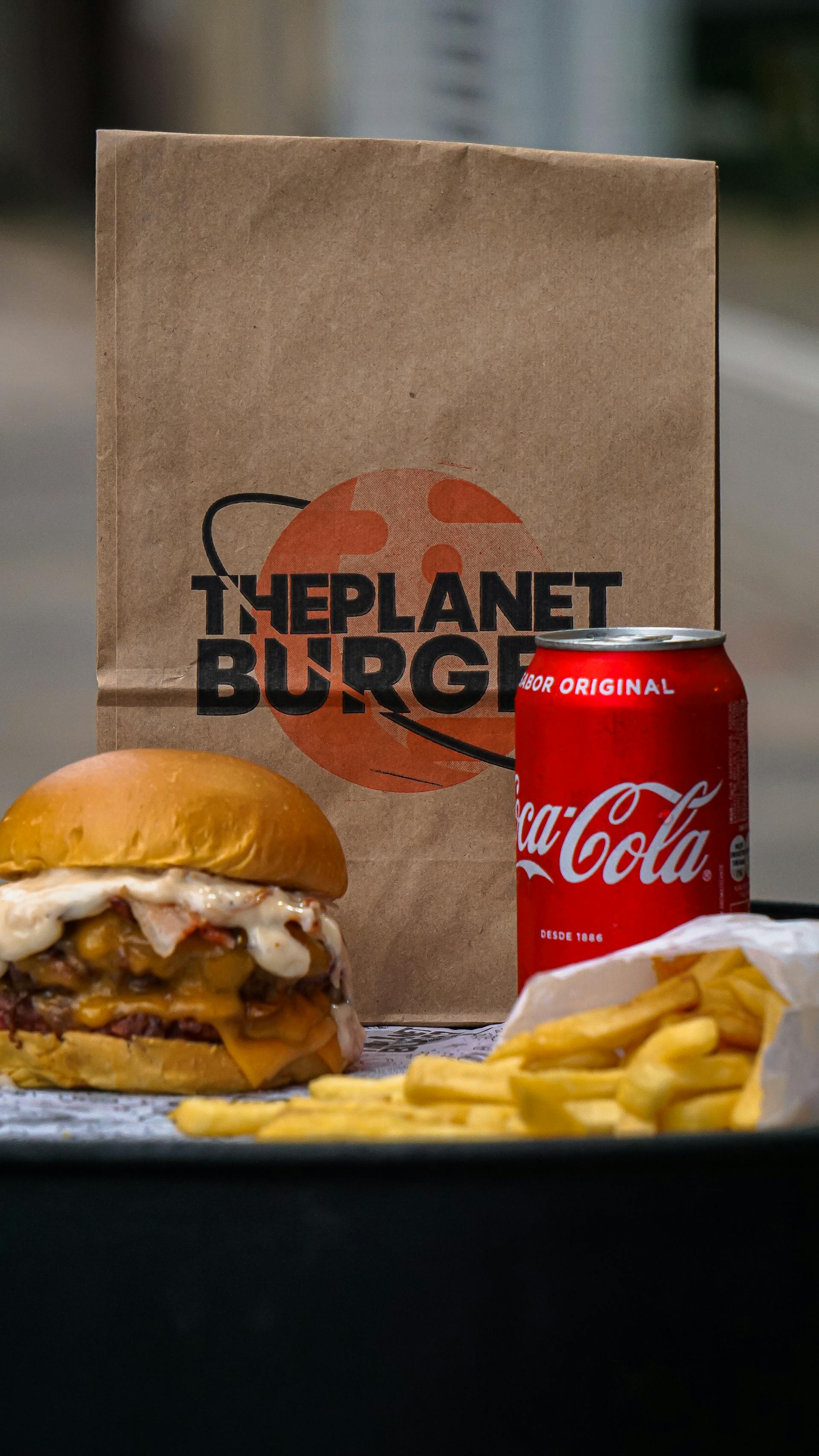 Una hamburguesa, patatas fritas y una lata de refresco junto a una bolsa de papel | Fuente: Pexels