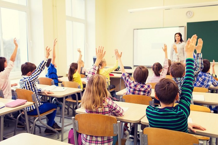Grupo de niños de la escuela con el maestro sentado en el aula y levantando las manos | Foto: Shutterstock
