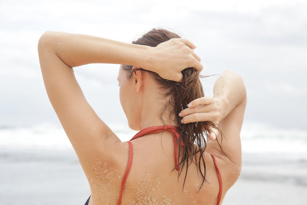 Mujer frotando su cabello en la playa bajo el sol. | Foto: Shutterstock