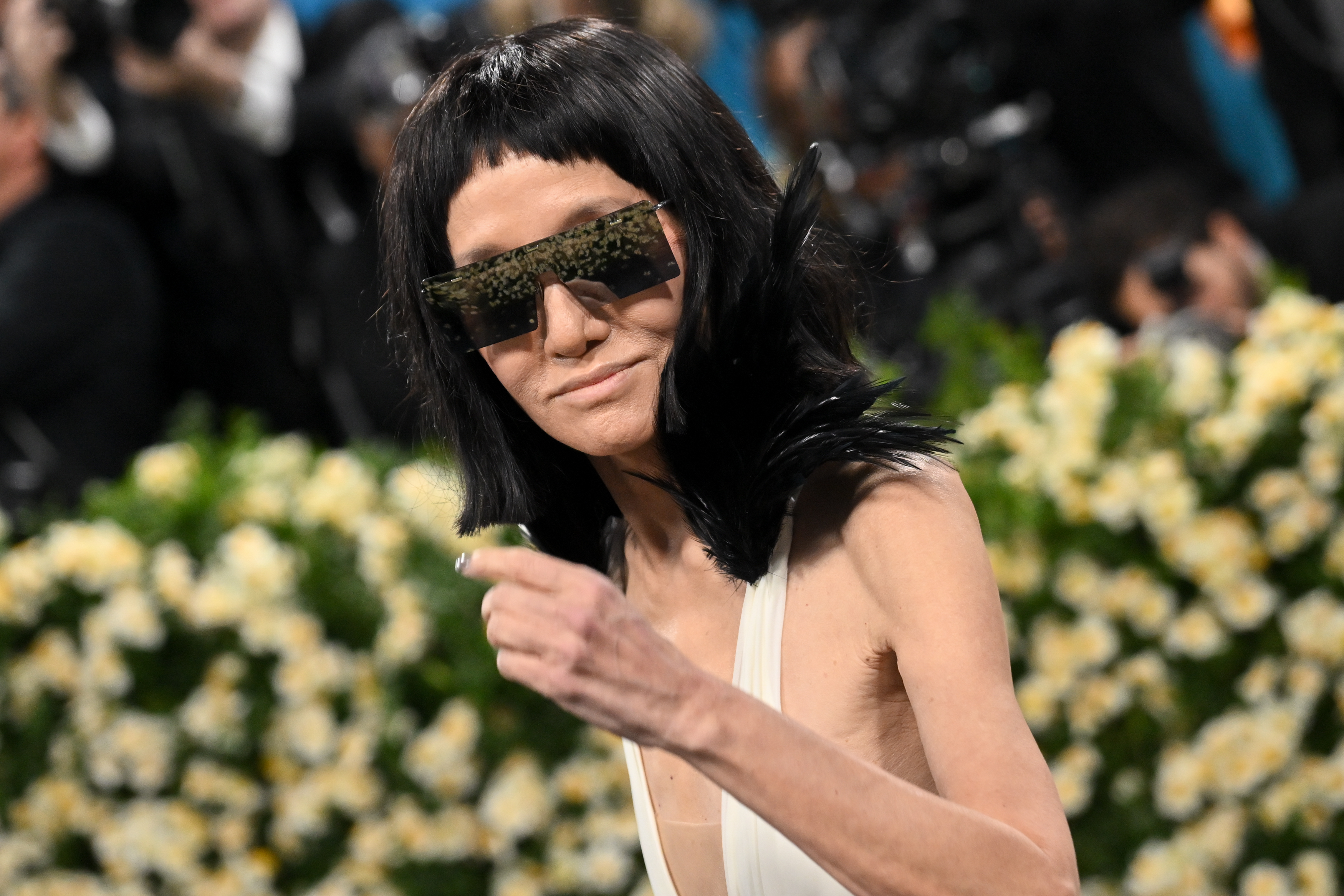 En un momento cándido, Vera Wang hace un gesto a la multitud mientras sus gafas de sol de espejo y su escote de plumas reflejan la energía de la noche.