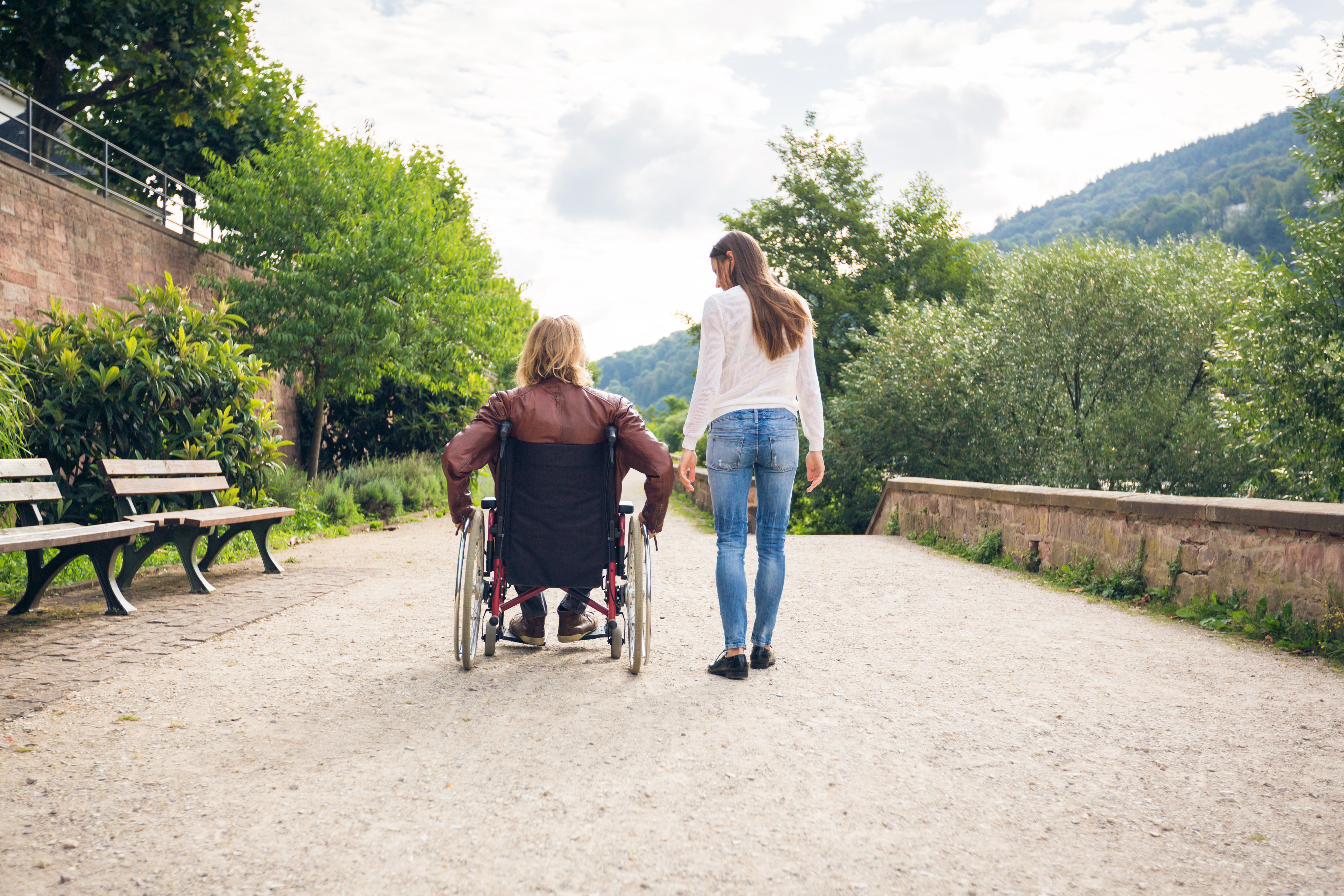 Hermana camina junto a hermano en silla de ruedas. | Foto: Shutterstock