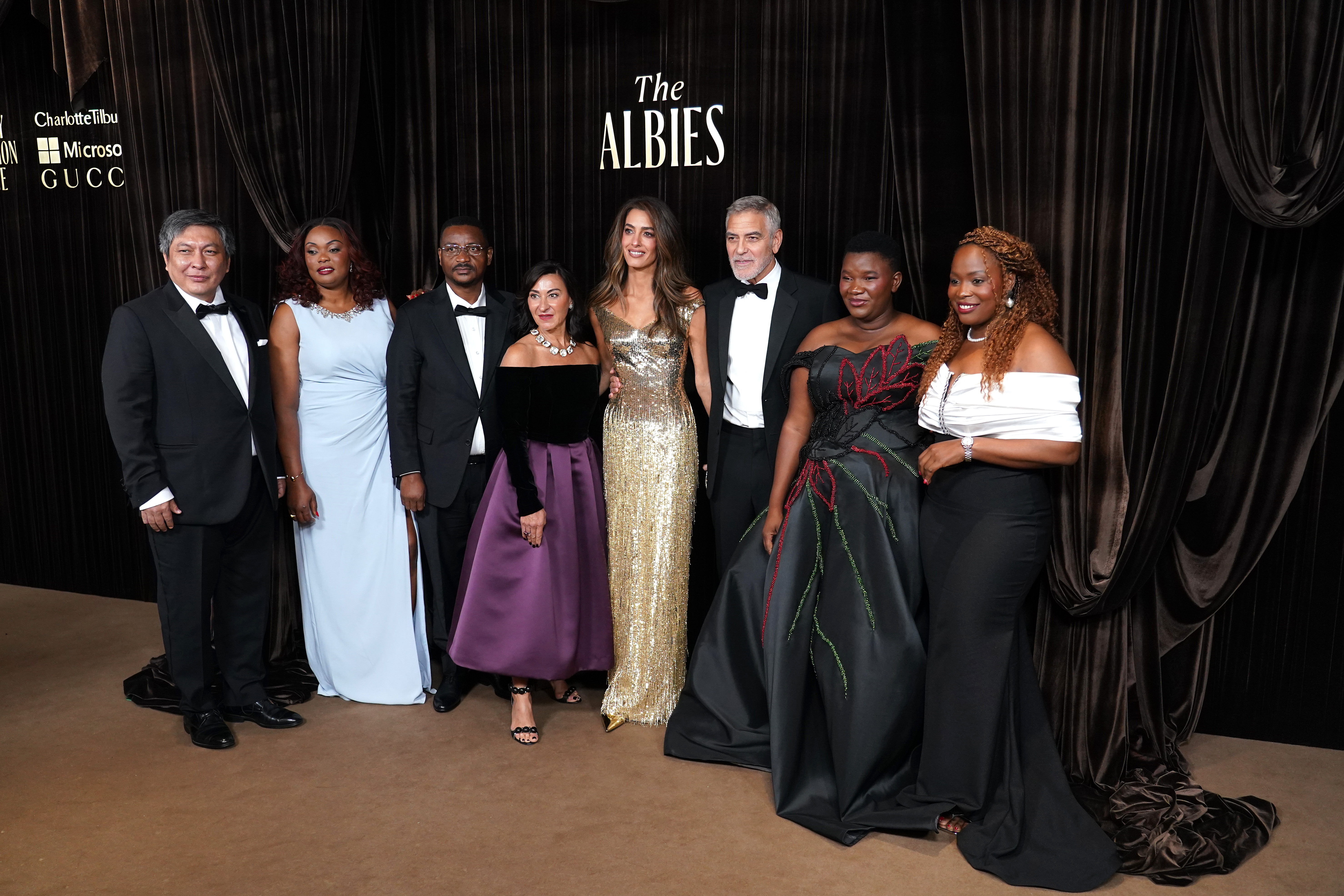 George Clooney y Amal Clooney posan con otros invitados e galardonados en los Albies 2026 de la Clooney Foundation for Justice en el Museo de Historia Natural de Londres el 9 de octubre. El grupo permanece de pie ante un fondo de cortinas negras con el logotipo de The Albies, vestidos con ropa formal de noche, con varias invitadas luciendo sus vestidos hasta el suelo. | Fuente: Getty Images