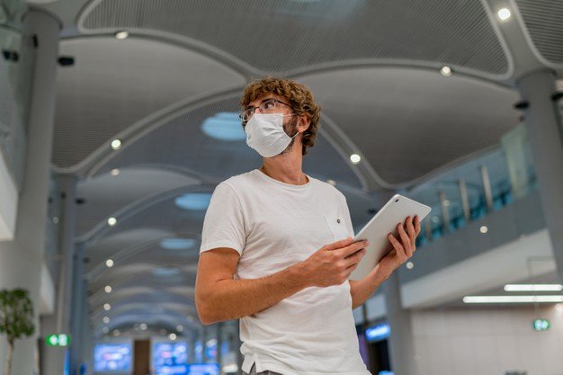 Hombre con mascarilla usando una tablet en un aeropuerto. │Foto: Freepik
