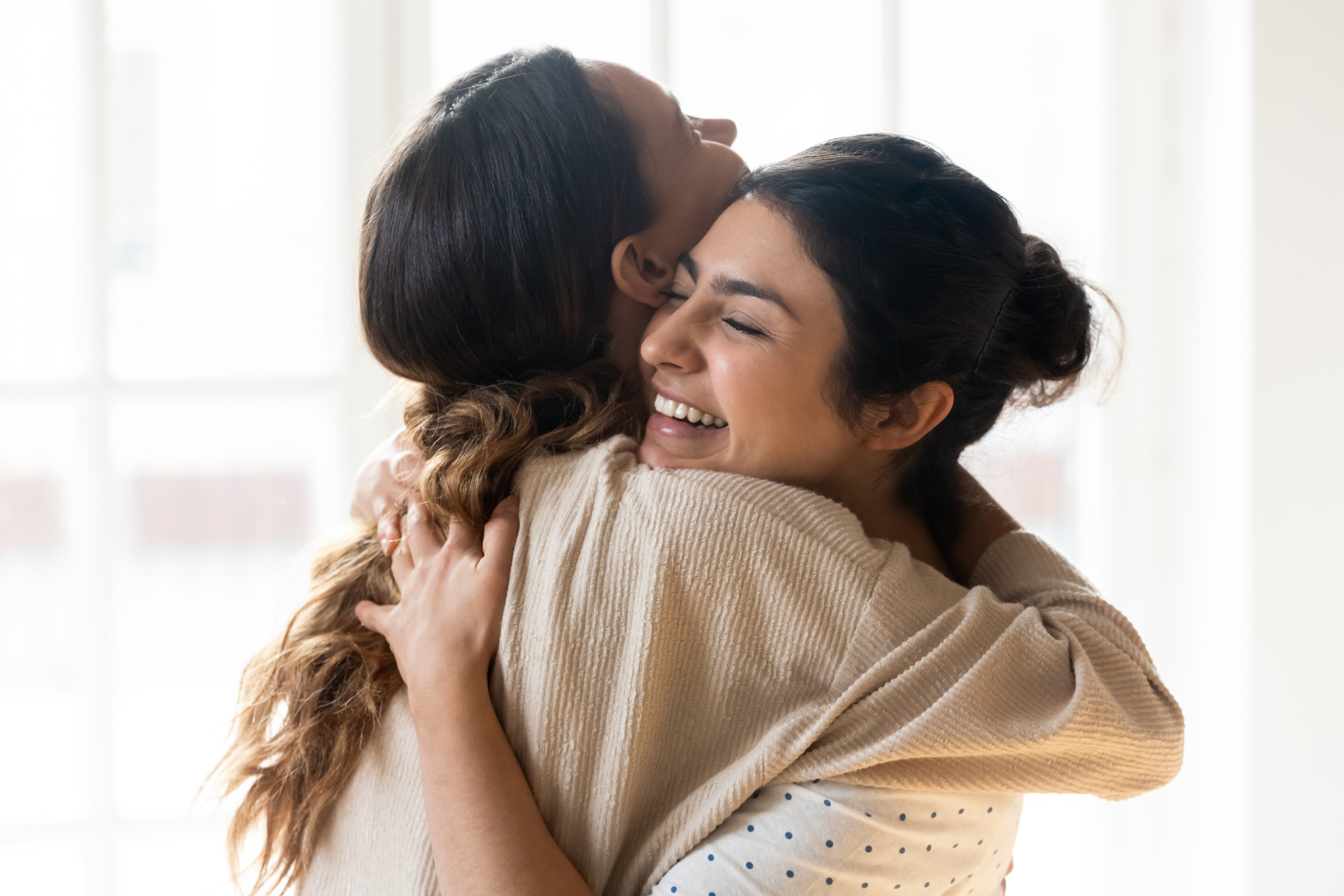 Cándidas chicas mejores amigas abrazándose de pie en un interior. | Fuente: Shutterstock