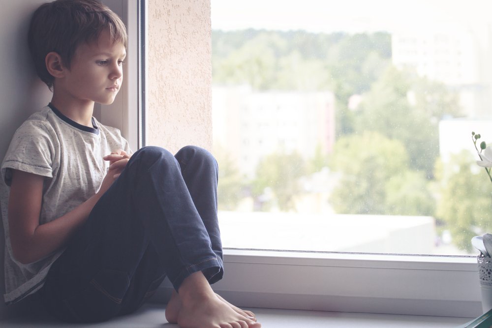 Niño triste sentado junto a una ventana. | Foto: Shutterstock