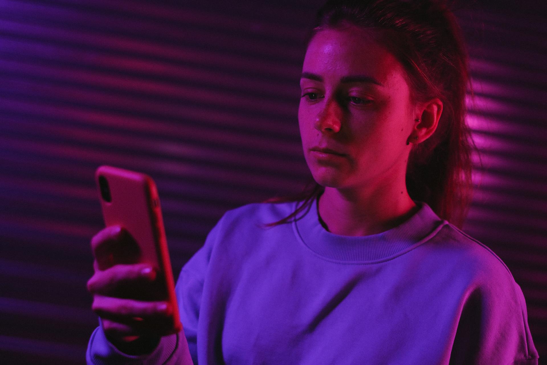 Una mujer usando su teléfono en una habitación oscura con luces de colores | Fuente: Pexels