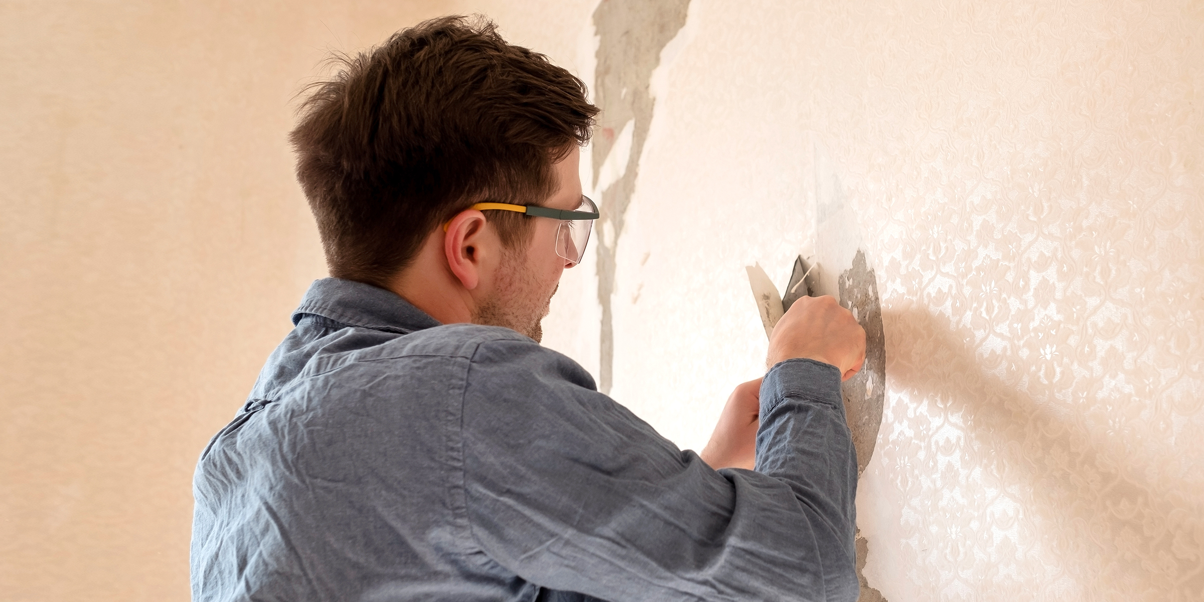 Un hombre despegando papel tapiz | Fuente: Shutterstock