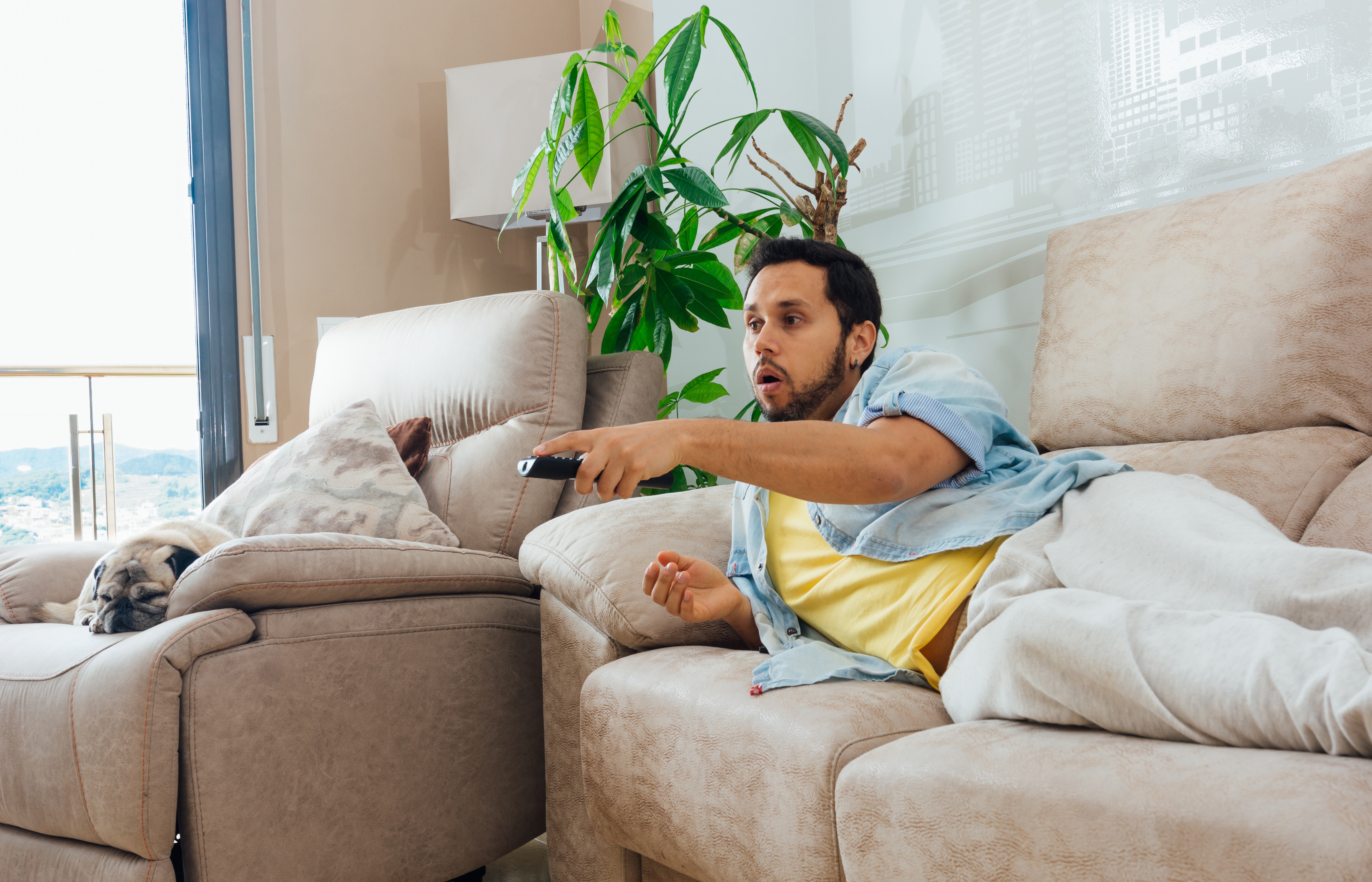 Hombre tumbado en un sofá con el mando de la tele | Fuente: wirestock on Freepik