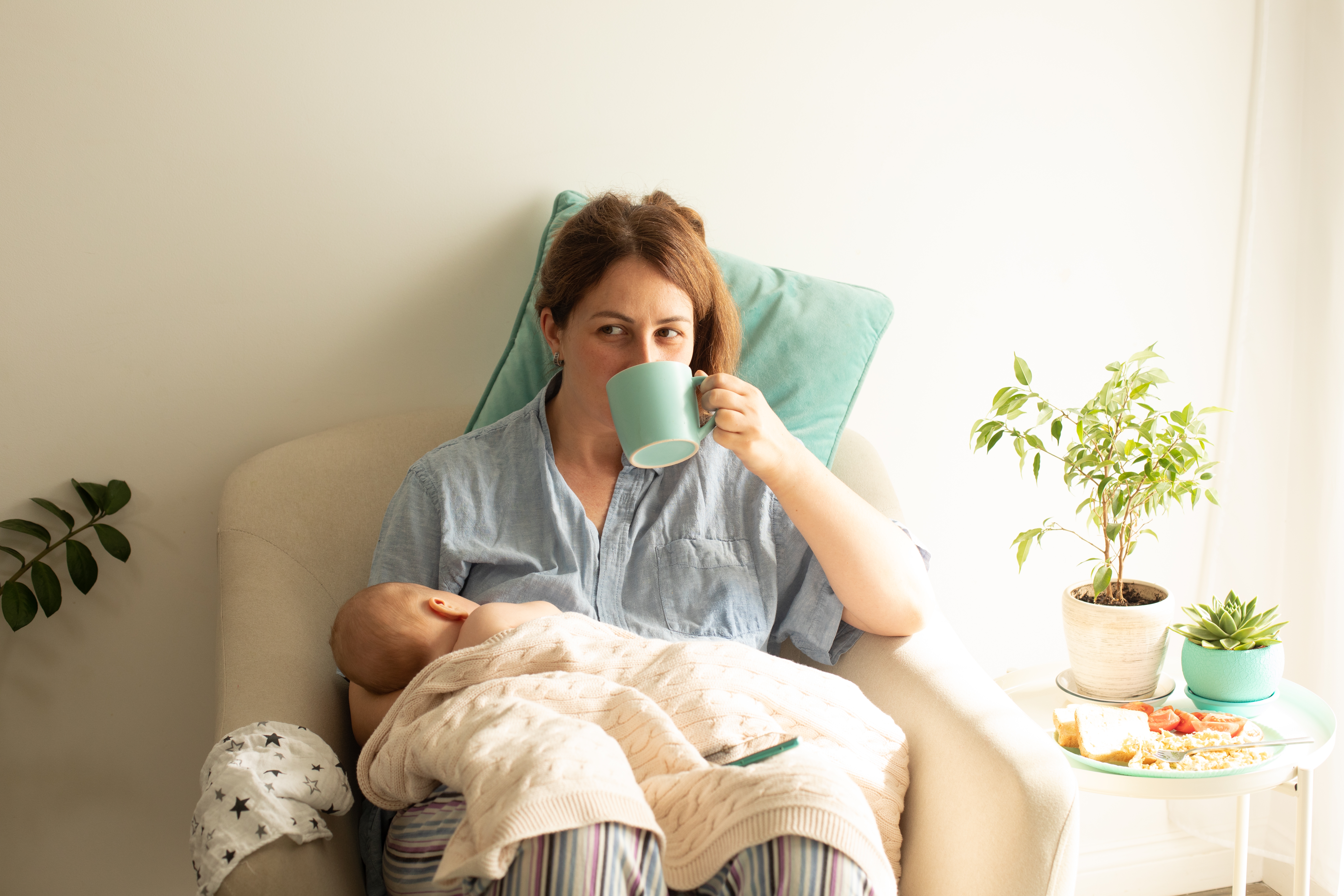 Una mujer amamanta a su recién nacido mientras bebe té | Foto: Shutterstock