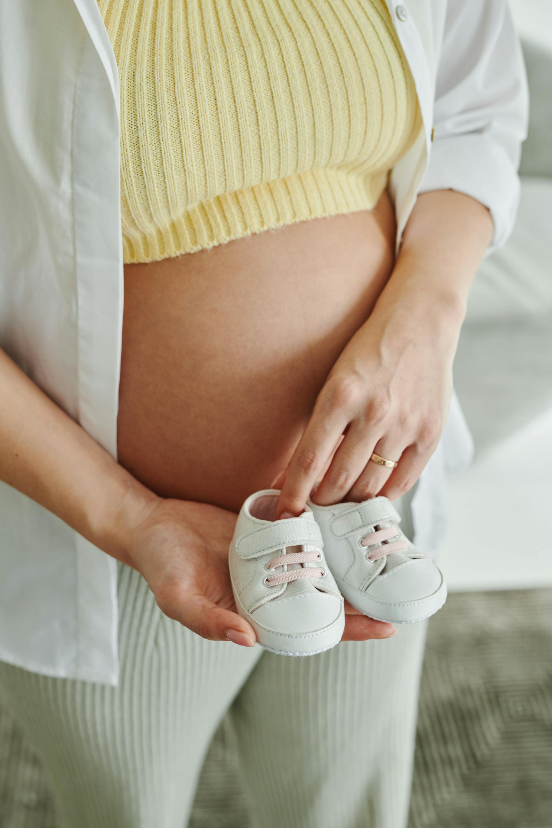 Una mujer embarazada con zapatos de bebé en la mano | Fuente: Pexels