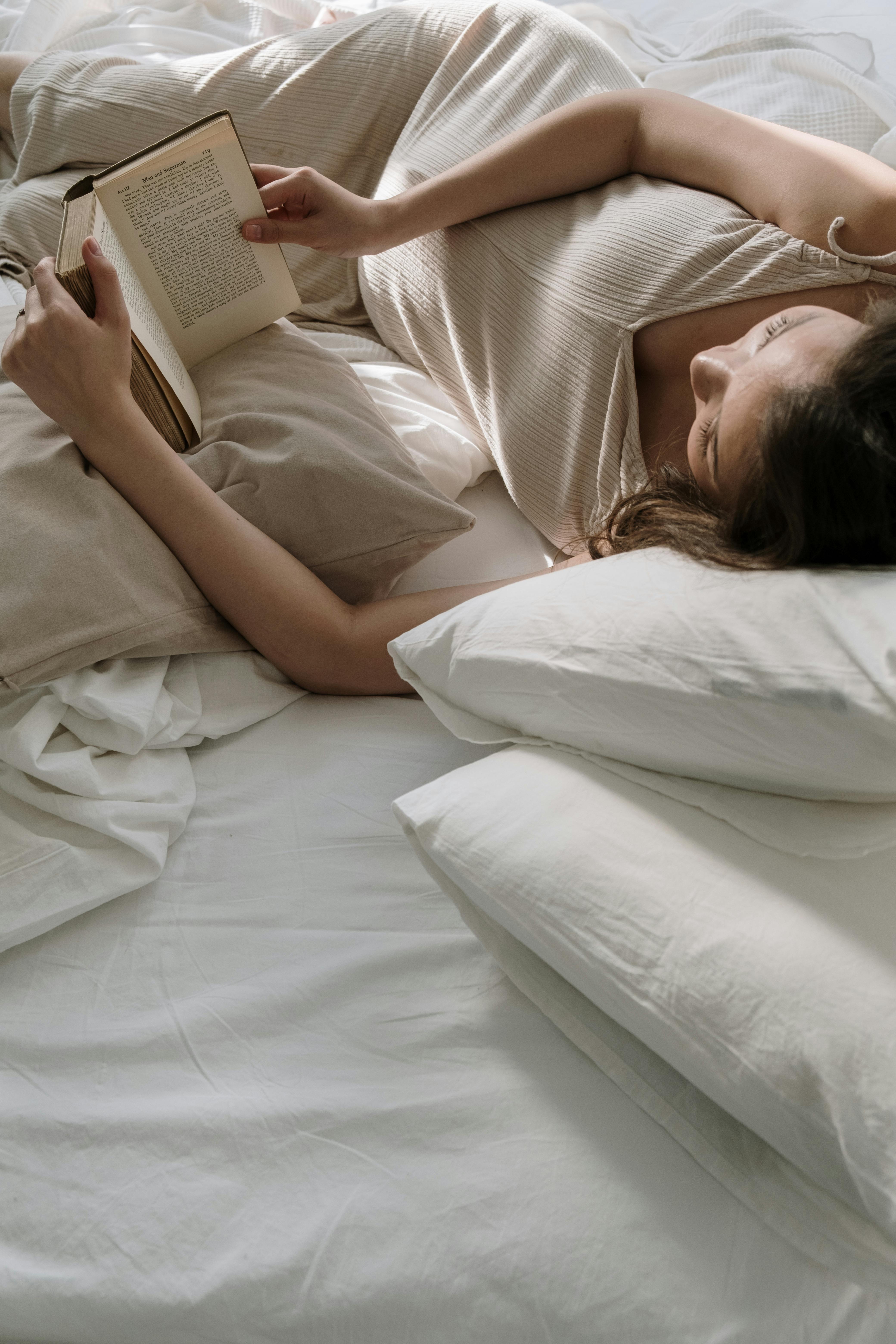 Una mujer tumbada en la cama leyendo un libro | Fuente: Pexels