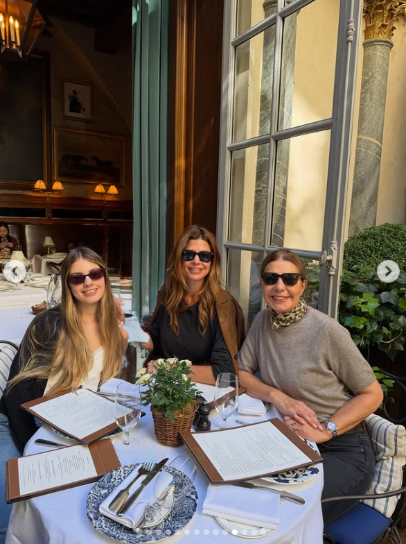 Juliana Awada disfruta de un almuerzo en París al aire libre junto a su hija Antonia Macri y una acompañante familiar, sentadas alrededor de una mesa redonda con mantelería blanca, vajilla decorada y lentes de sol oscuros. | Fuente: Instagram/juliana.awada