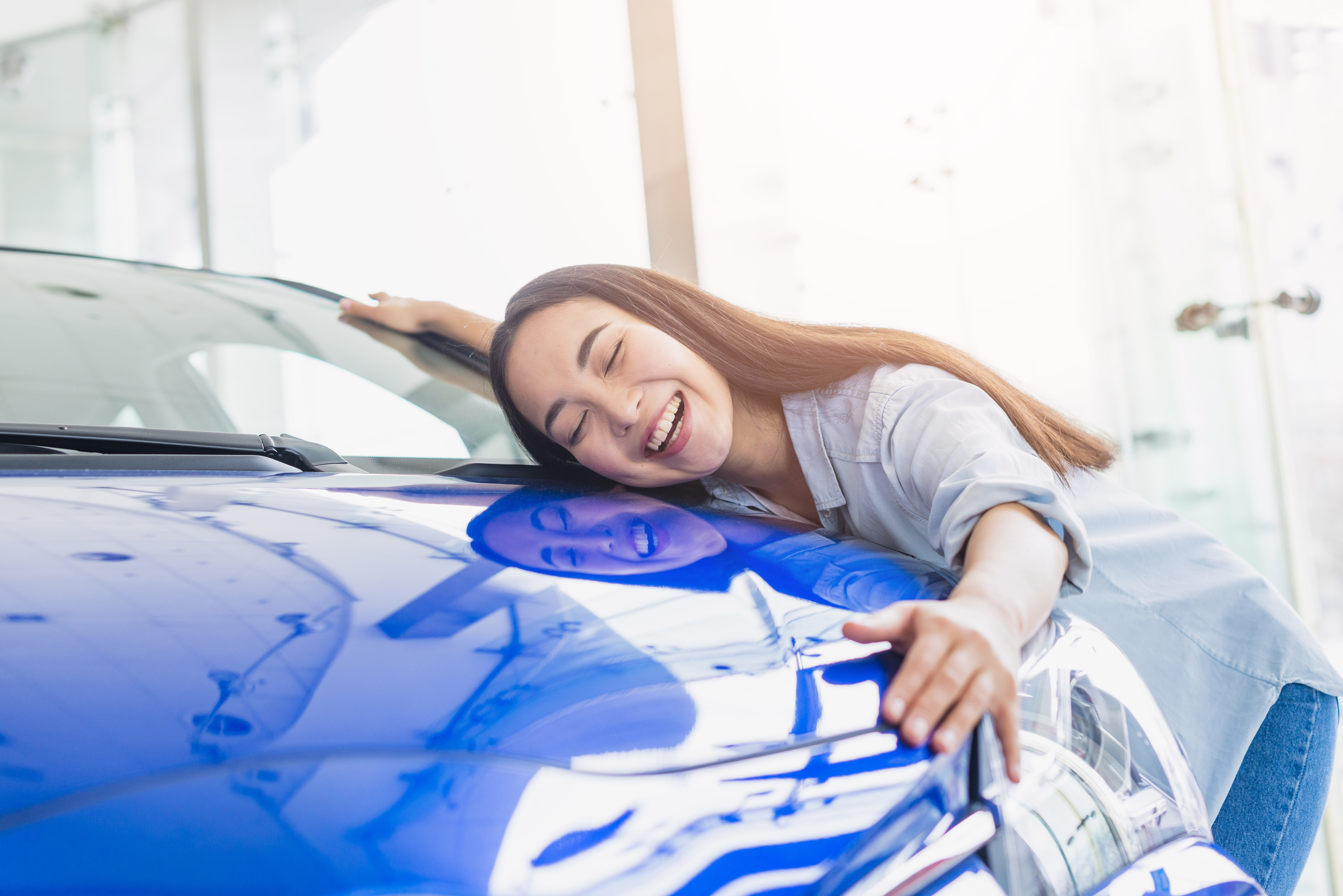 Una joven abrazando el capó de un Automóvil azul | Fuente: Freepik