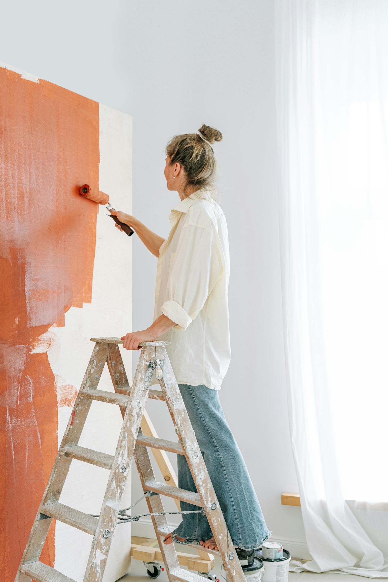 Una mujer de pie en una escalera y pintando una pared | Fuente: Pexels
