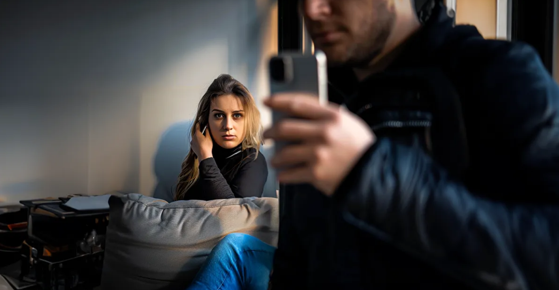 Mujer espiando detrás de un hombre con un teléfono | Foto: Shutterstock