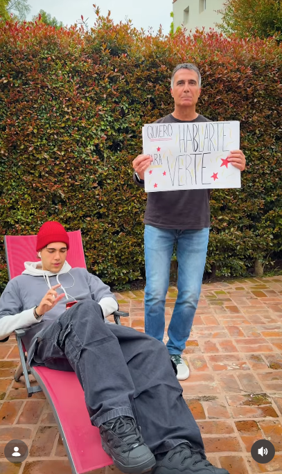 Antonio Laje sostuvo con ambas manos el primer cartel del video promocional con la frase manuscrita "QUIERO HABLARTE PARA VERTE" decorada con estrellas rojas. En la parte inferior, su hijo Leish revisaba concentrado su celular recostado en una reposera roja con un look urbano. | Fuente: Instagram/leish.ar