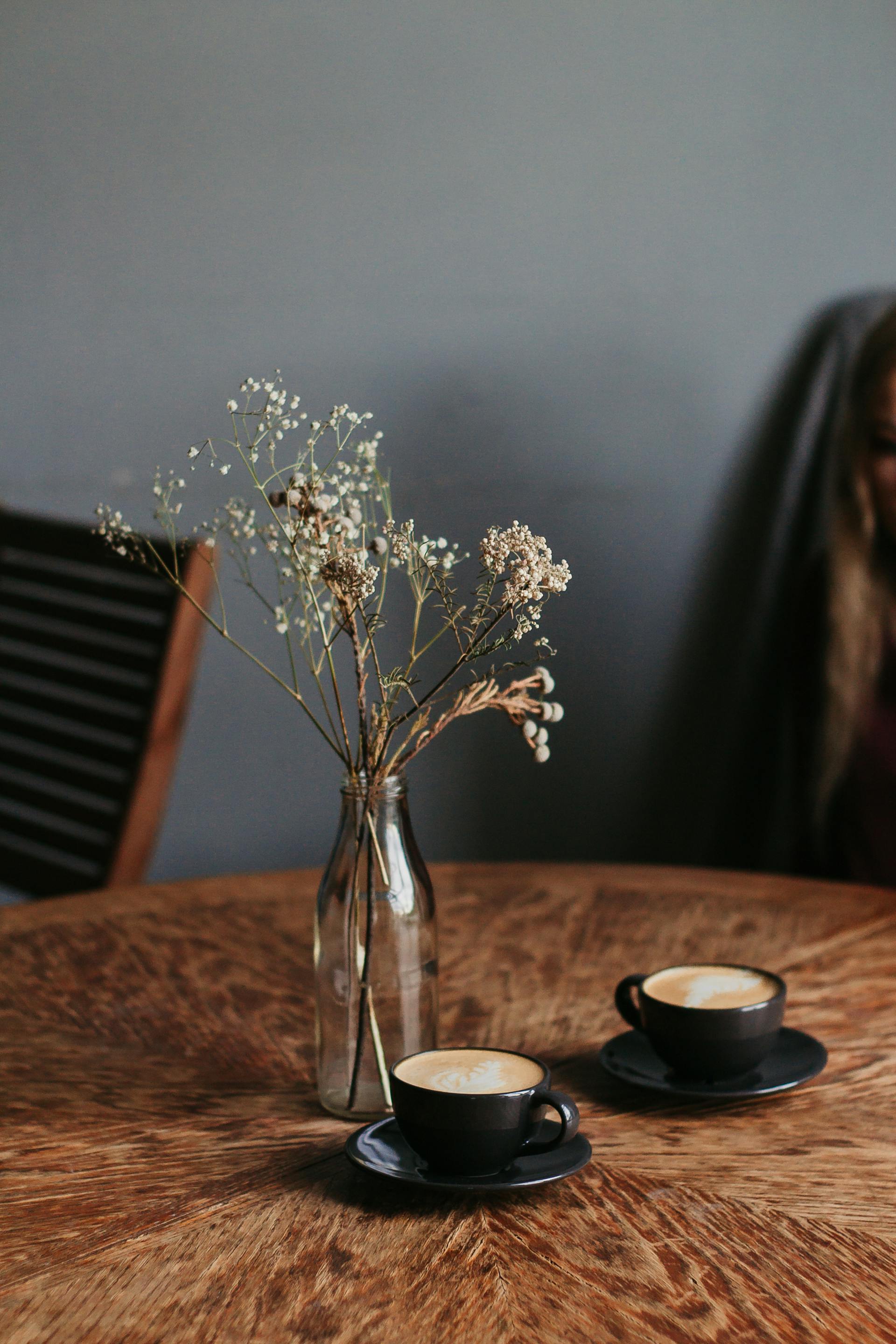 Dos tazas de café cerca de un jarrón de flores sobre una mesa | Fuente: Pexels