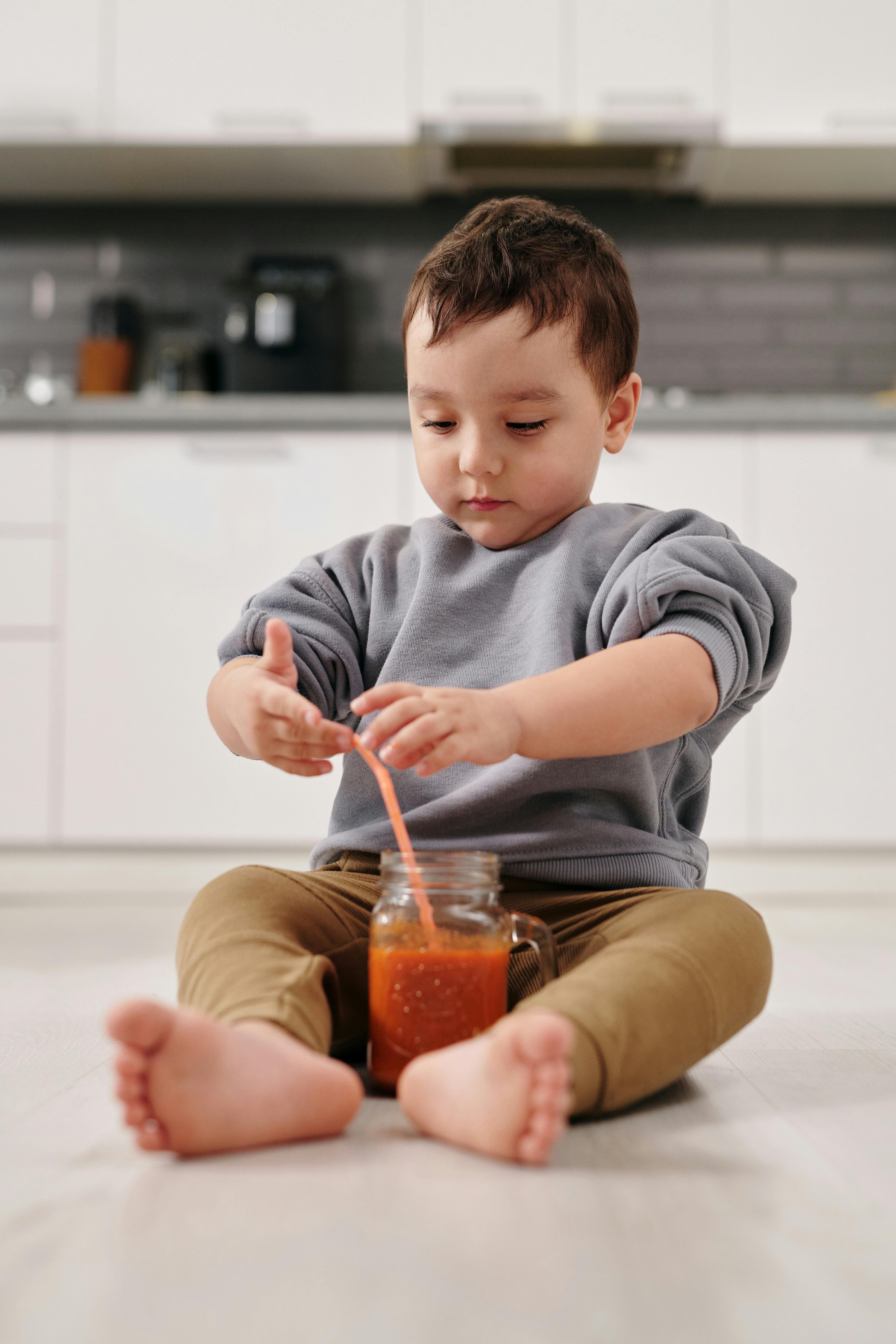 Un niño sentado en el suelo junto a un vaso de jugo | Fuente: Pexels