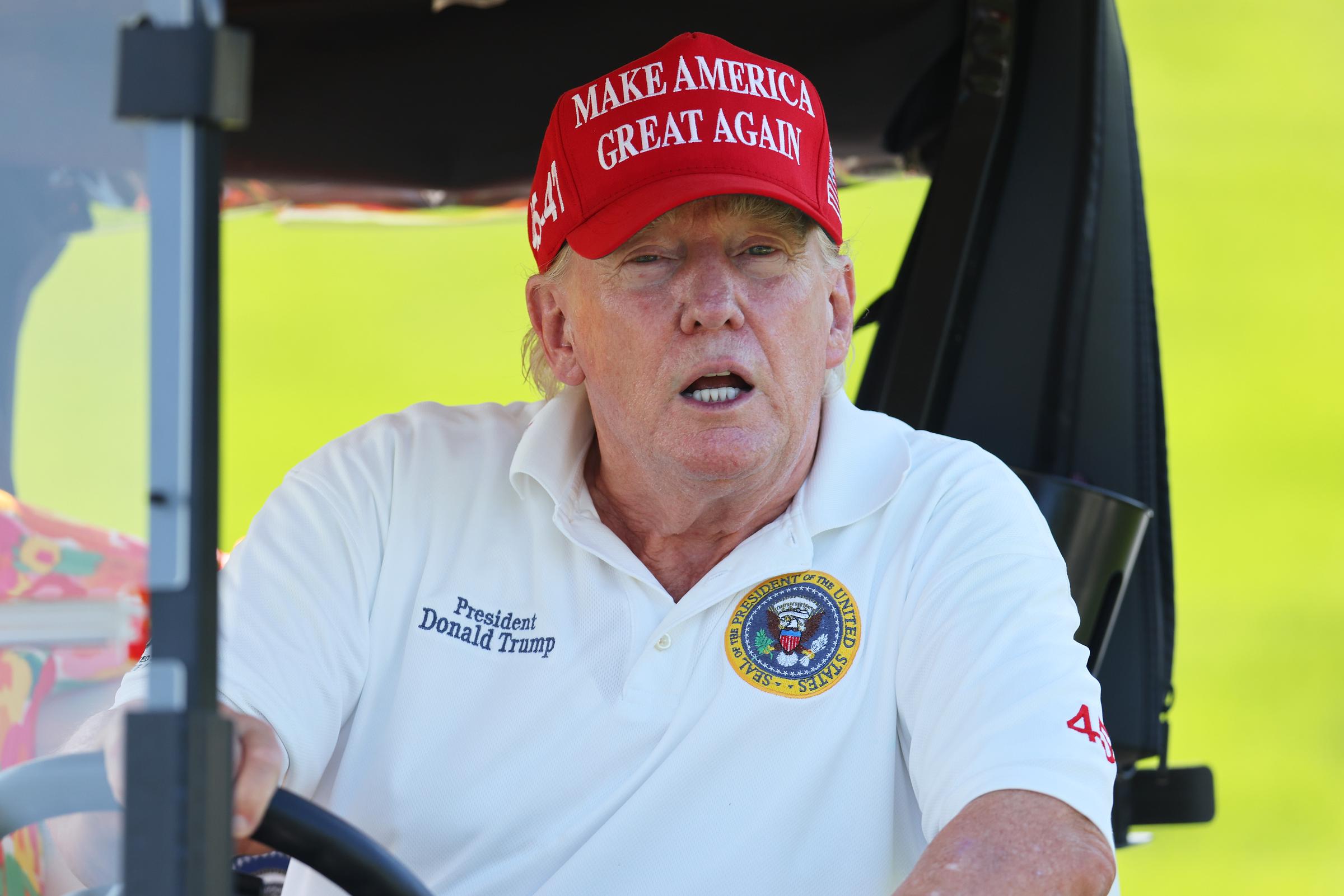 En el acto de Bedminster, en Nueva Jersey, el 11 de agosto, Donald Trump está sentado dentro de un carrito de golf vestido con un polo blanco con el emblema presidencial. Su cara parece más roja que su cuello, sobre todo bajo la brillante luz exterior.