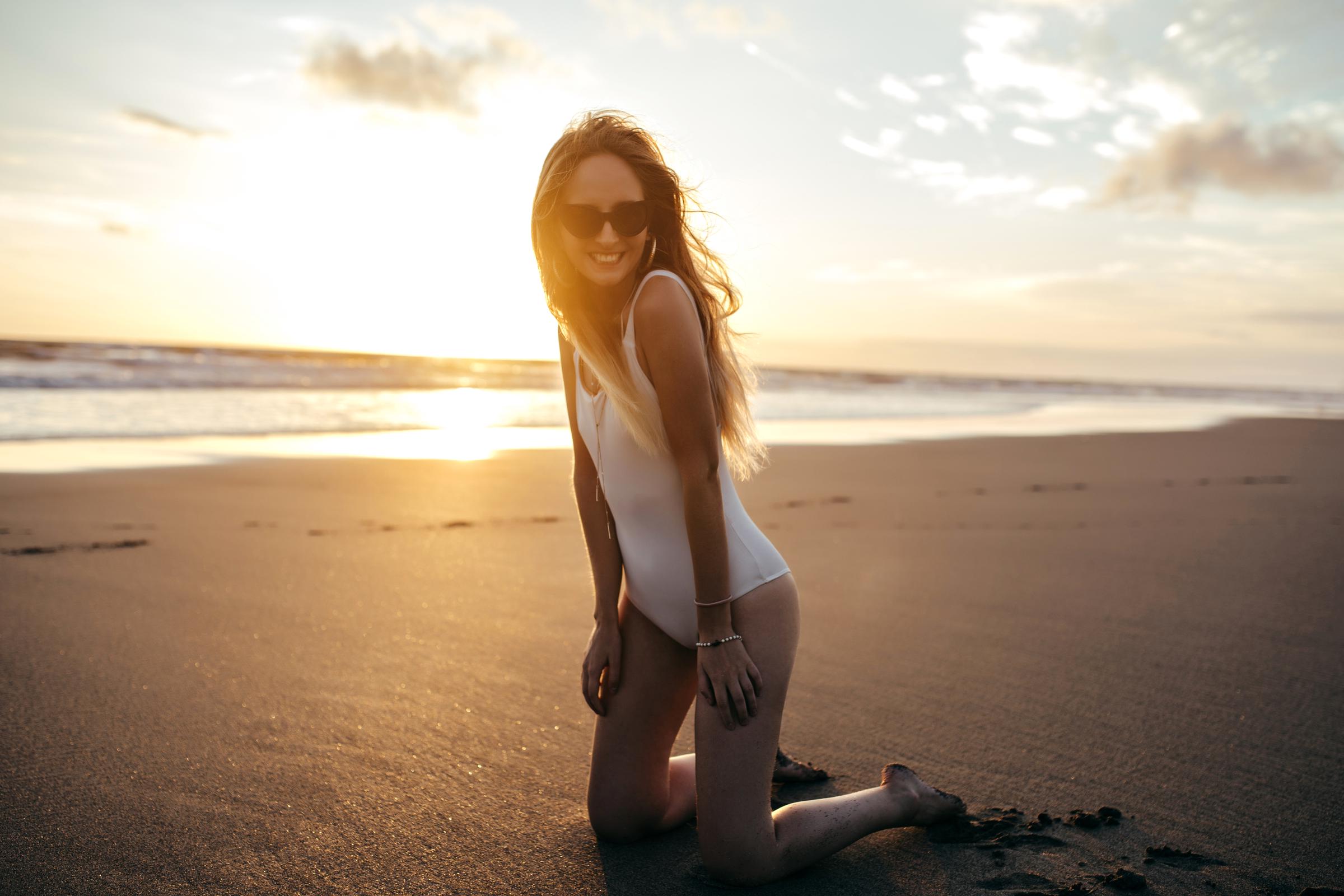 Una mujer en bañador blanco arrodillada en la playa | Fuente: Freepik