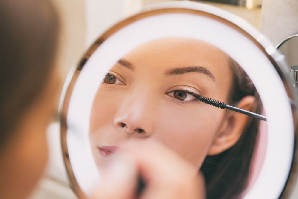 Mujer maquillándose los ojos con un espejo de aumento. | Foto: Shutterstock