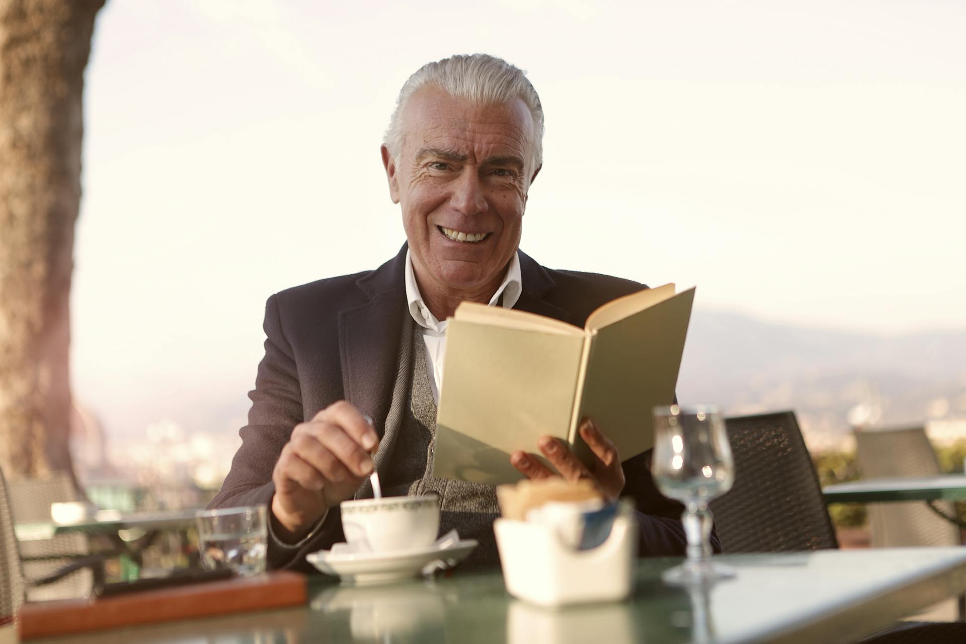 Un hombre sentado en una mesa y sonriendo mientras sostiene un libro | Fuente: Pexels