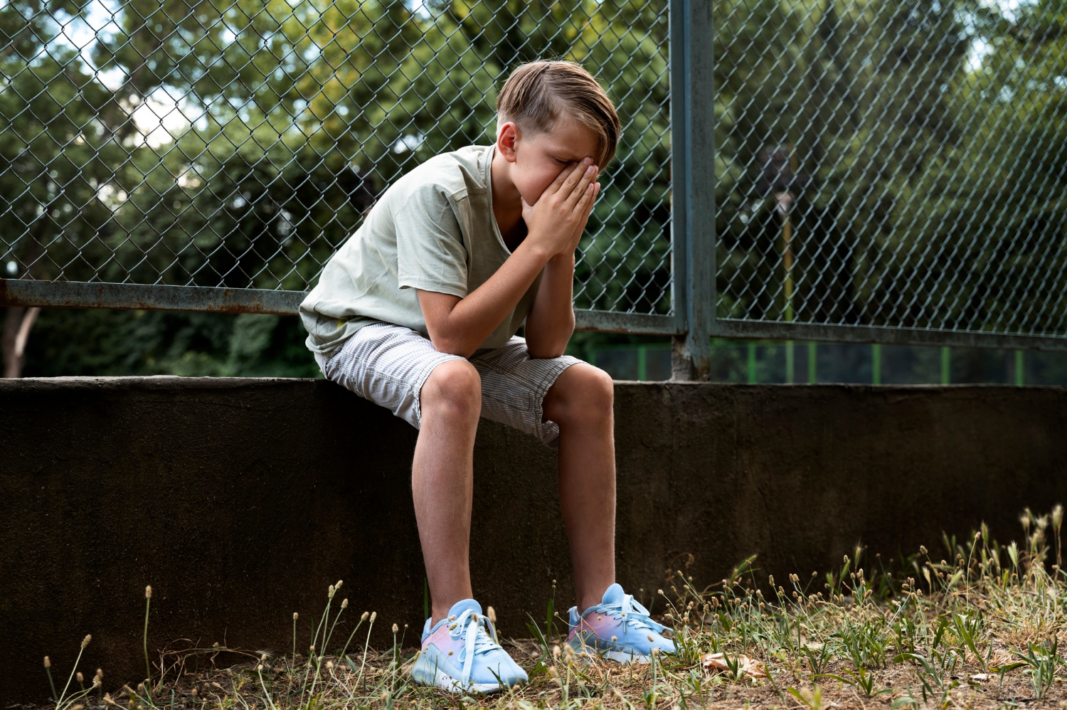 Un niño con el corazón roto sentado en el muro de una valla baja | Fuente: Freepik