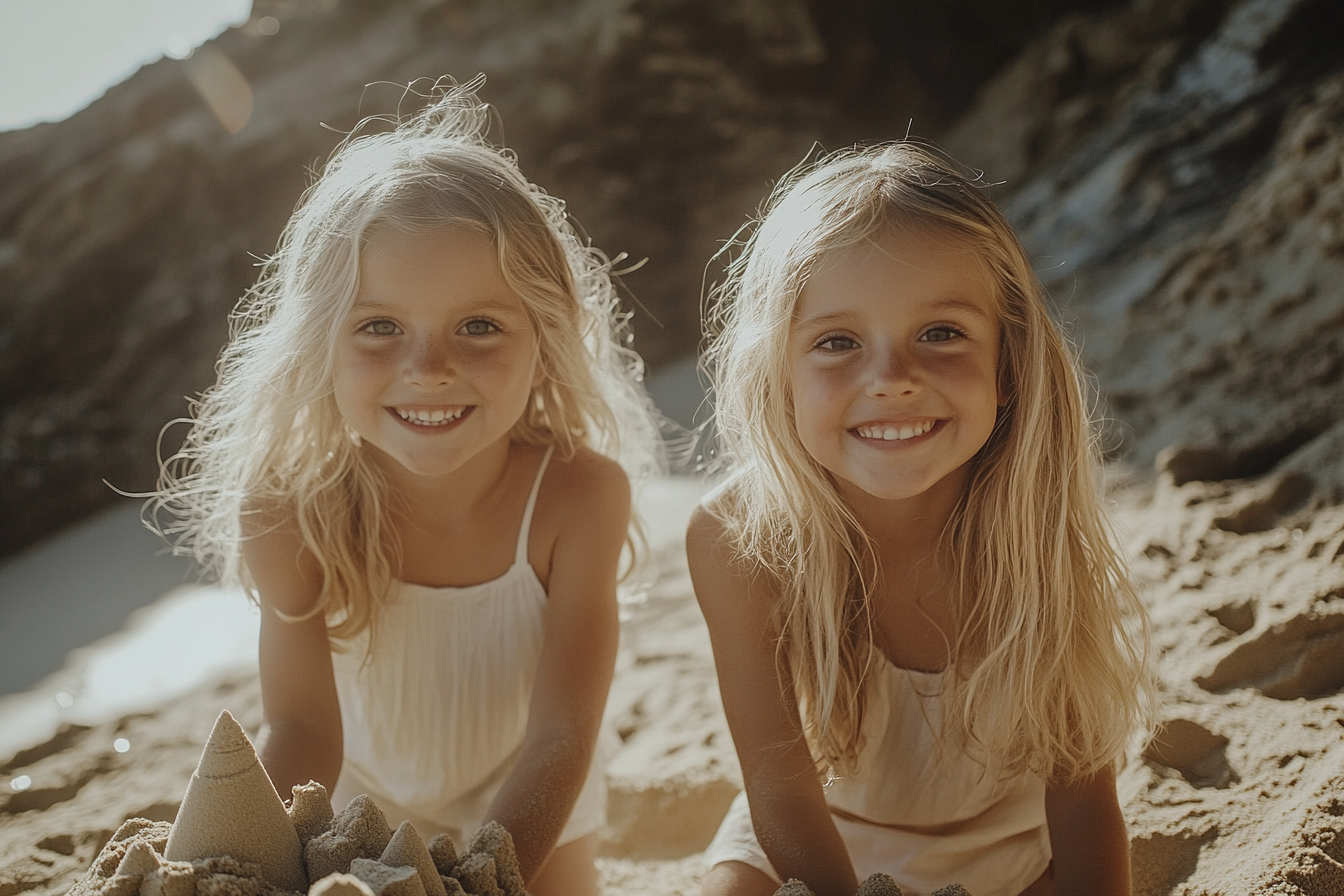 Gemelas sonriendo y construyendo un castillo de arena en la playa | Fuente: Midjourney