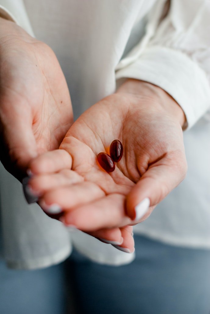 Mujer con dos píldoras oscuras en su mano. | Foto: Unsplash