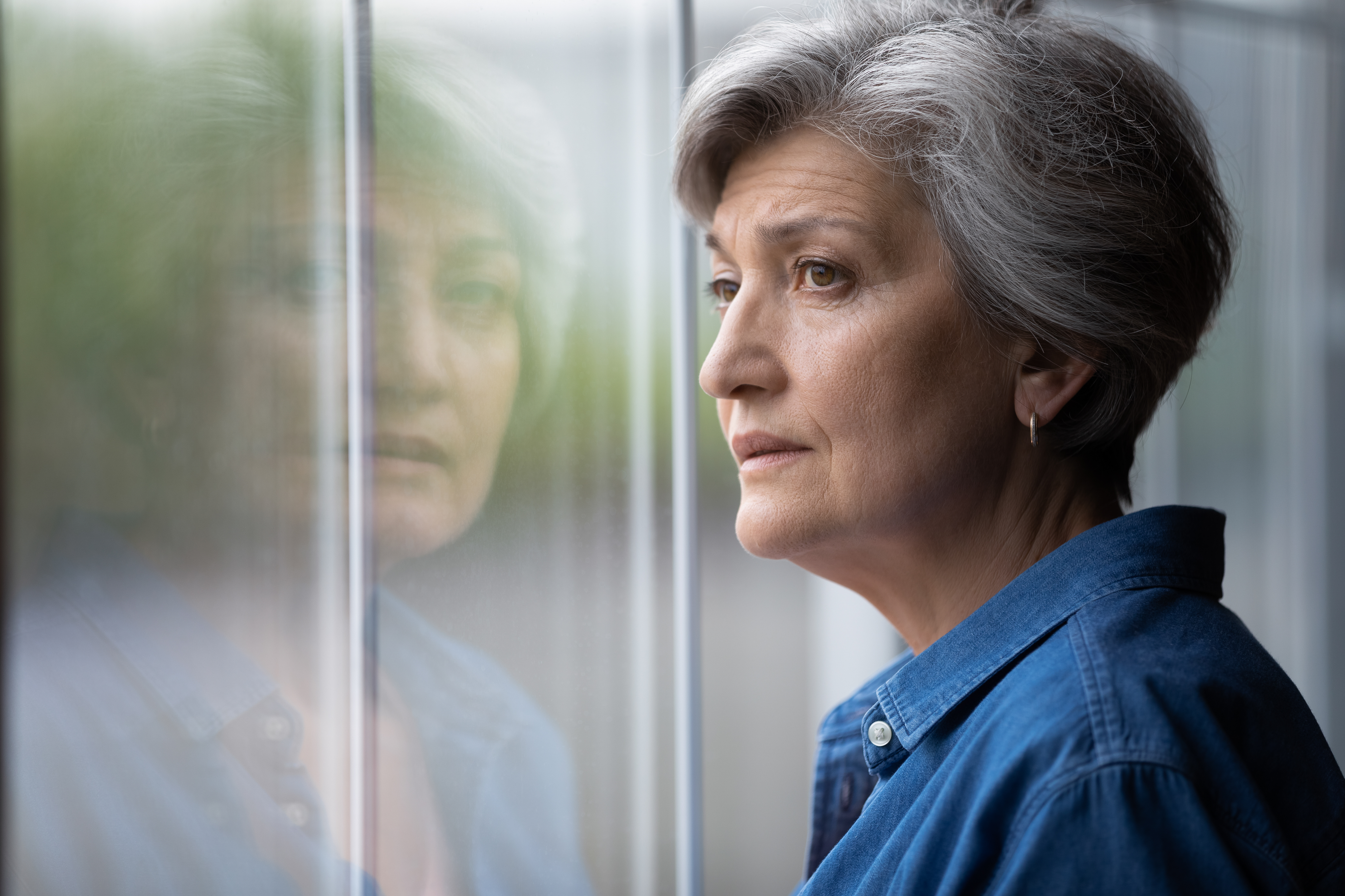 Una señora mayor ansiosa mirando por la ventana | Foto: Shutterstock