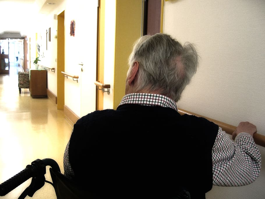 Anciano en silla de ruedas se sostiene de la baranda en un pasillo. | Foto: Piqsels