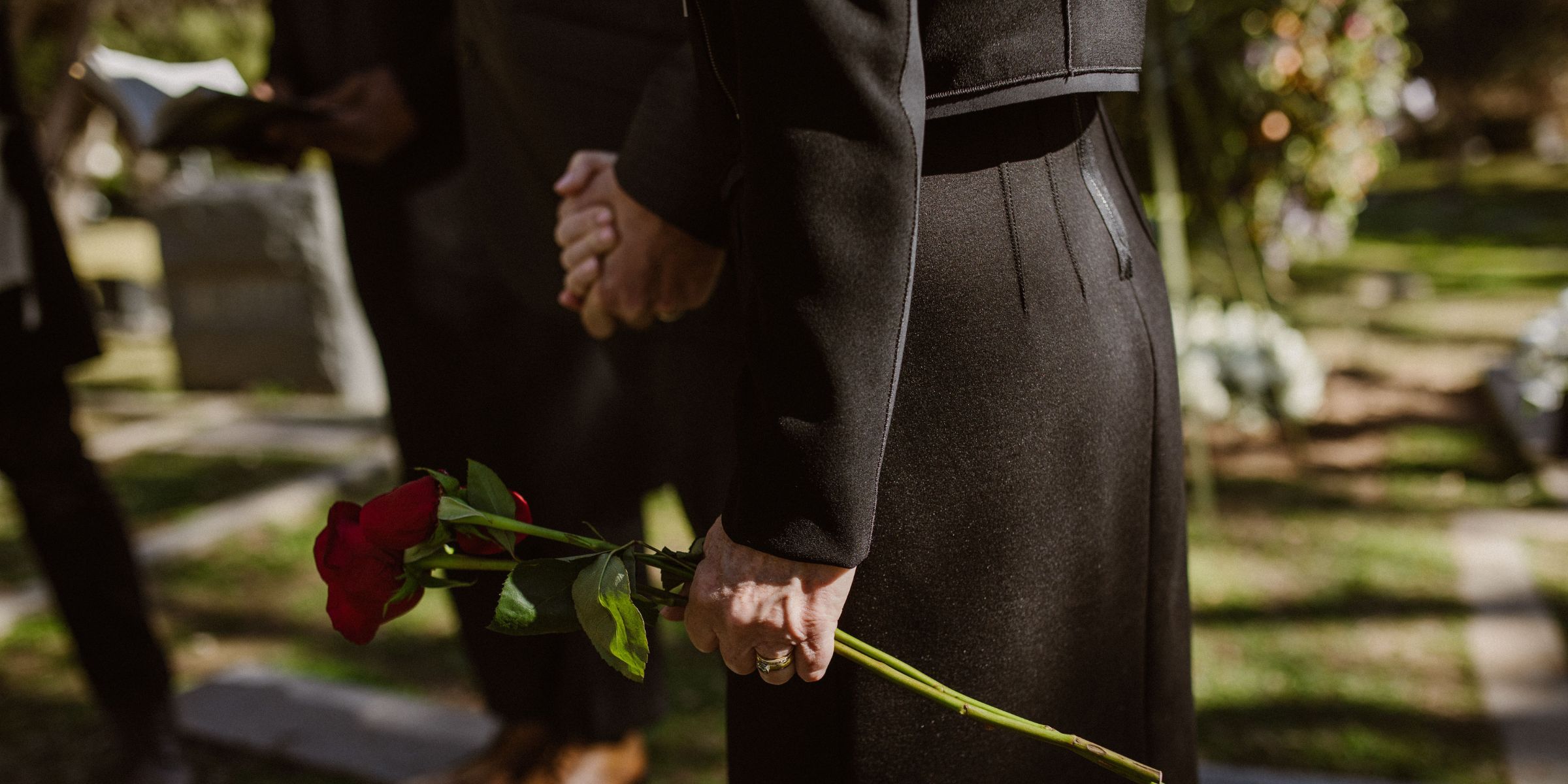 Un primer plano de una mujer vestida de negro que sostiene una rosa roja en un cementerio | Fuente: Pexels