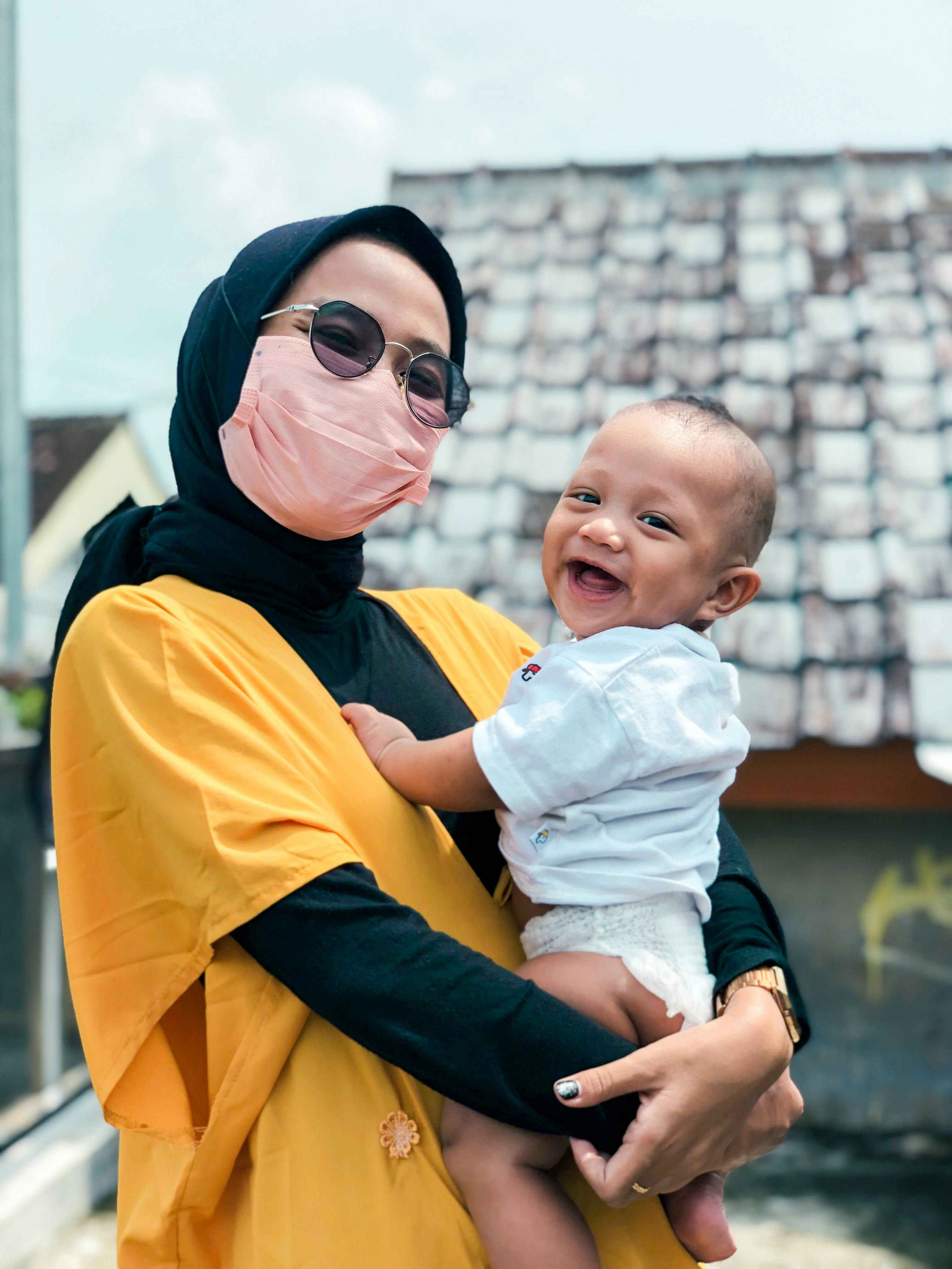 Una mujer con una máscara y un bebé sonriente en brazos | Foto: Pexels