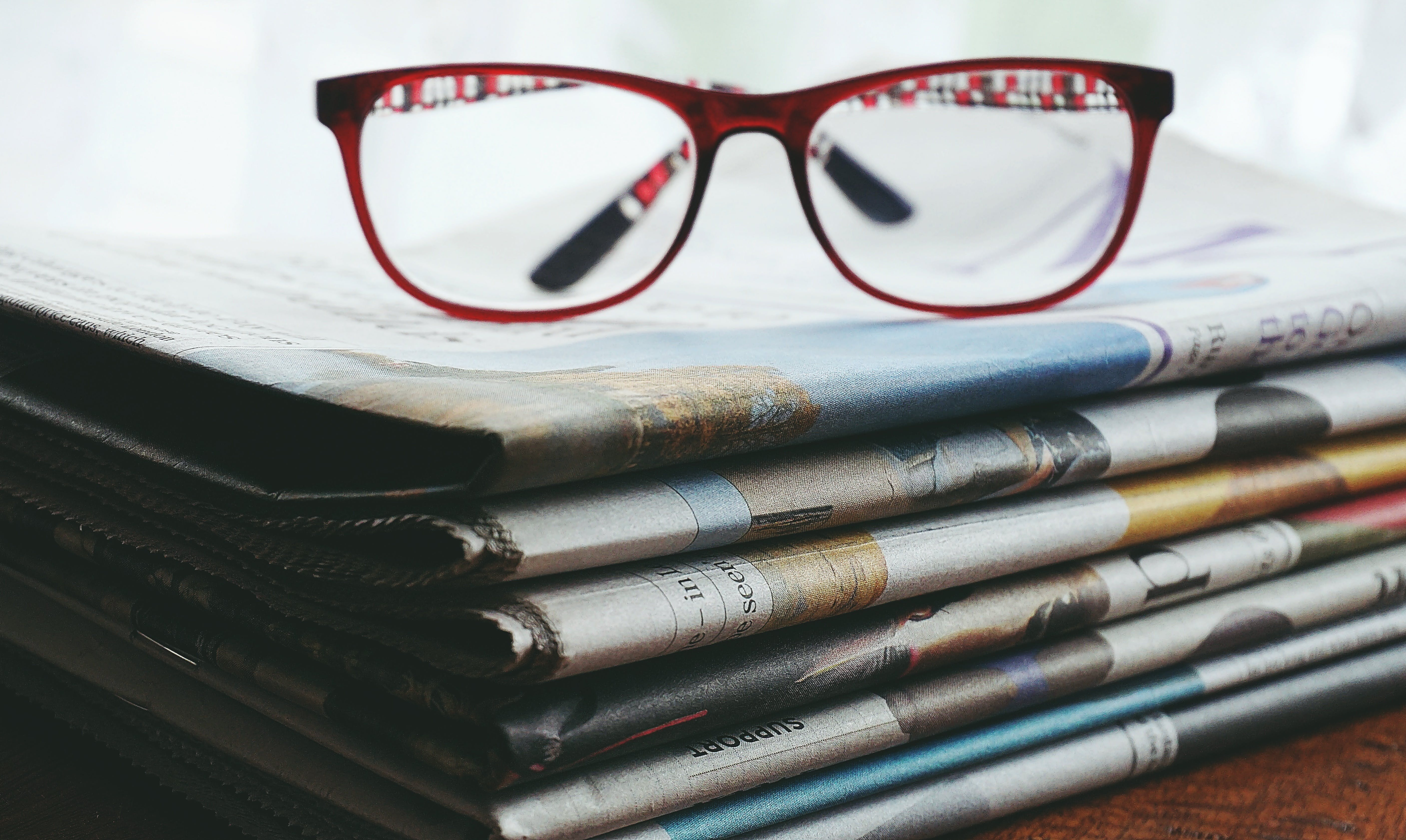 Gafas con marco rojo en los periódicos. | Fuente: Pexels