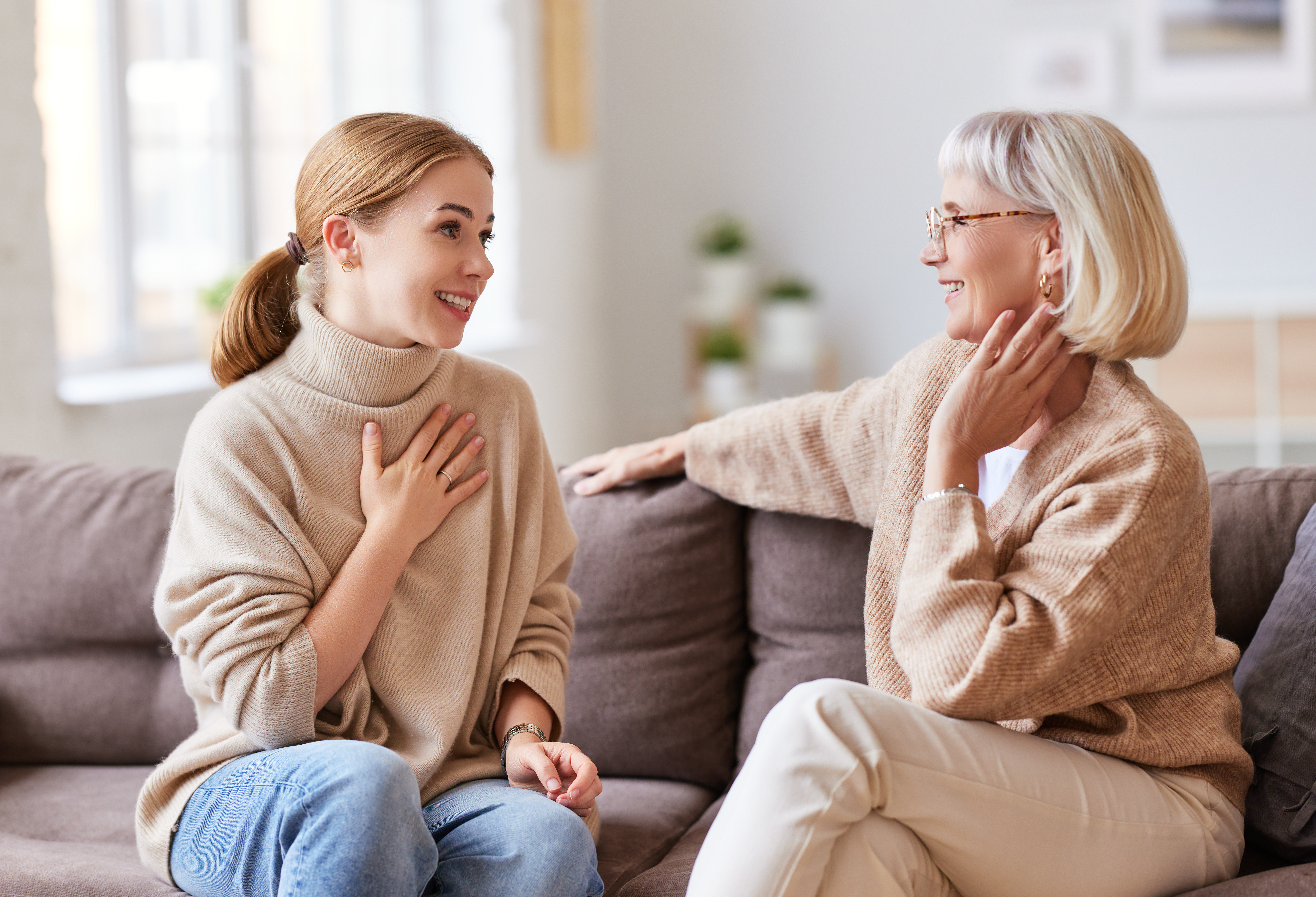 Una mujer joven sonríe mientras habla con otra mayor sentada en un sofá. | Foto: Shutterstock