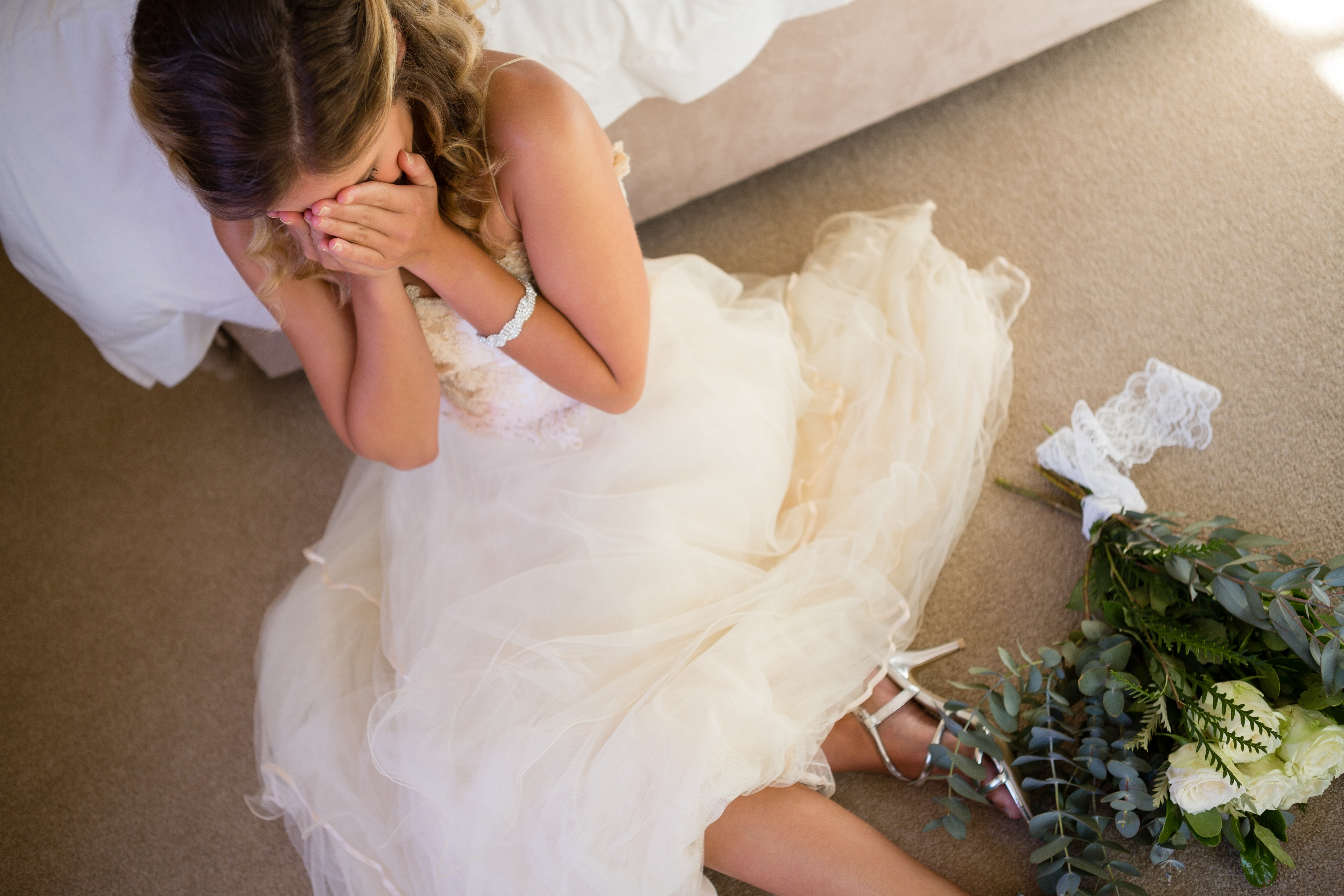 Una novia llora en el suelo mientras se apoya en una cama. | Foto: Shutterstock
