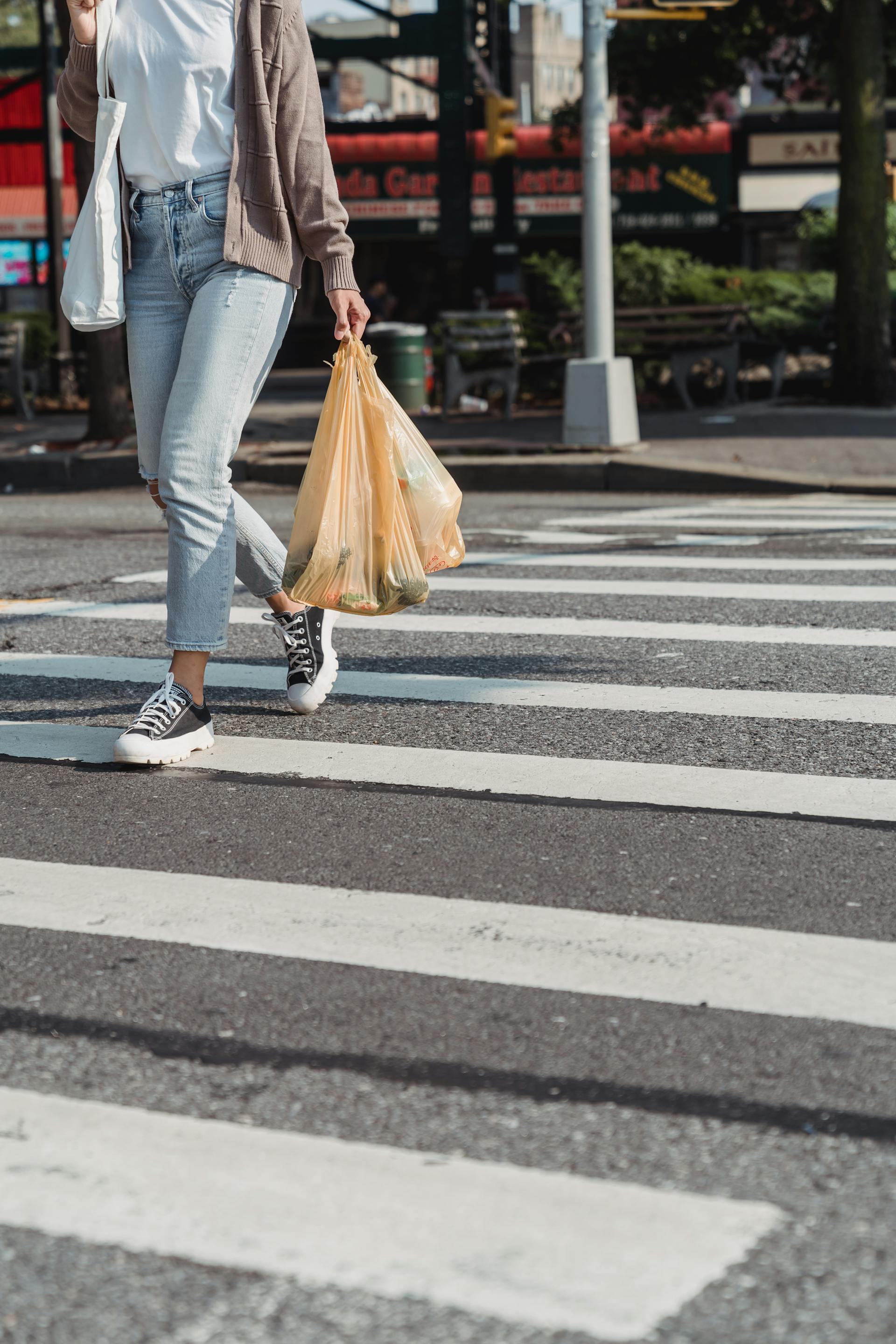 Una mujer caminando por un paso de cebra con bolsas de la compra | Fuente: Pexels