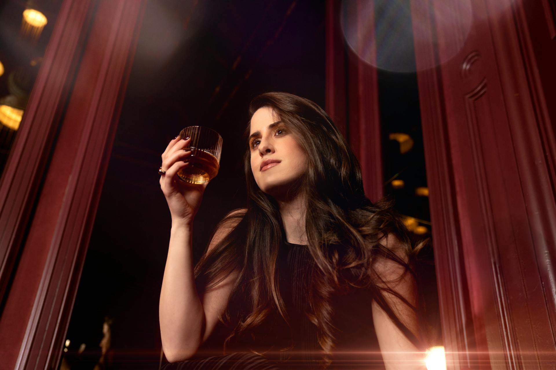 Un plano de ángulo bajo de una mujer con un vaso de whisky en la mano | Fuente: Pexels