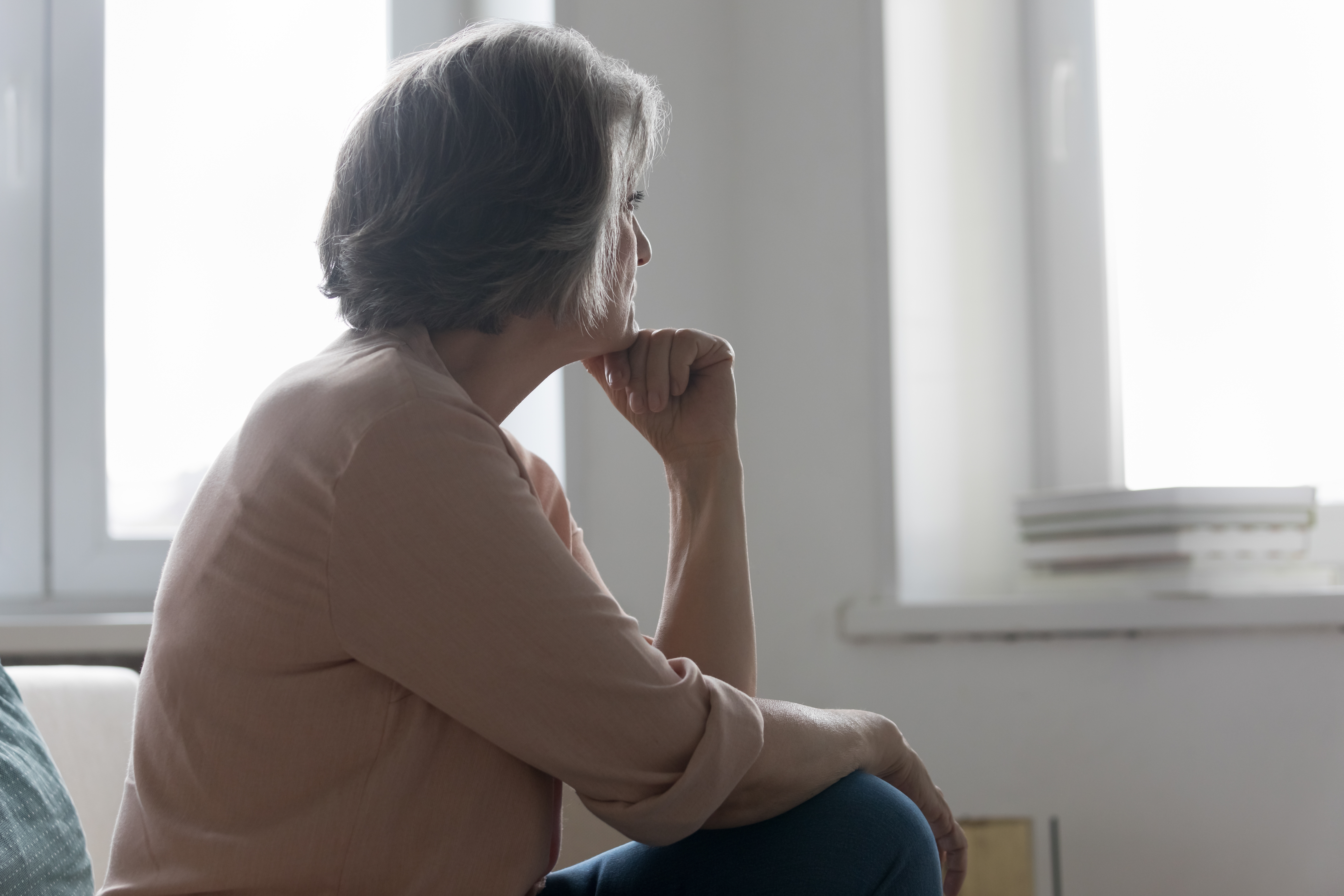 Una mujer mayor sentada en una cama y mirando al exterior pensativa. | Foto: Shutterstock